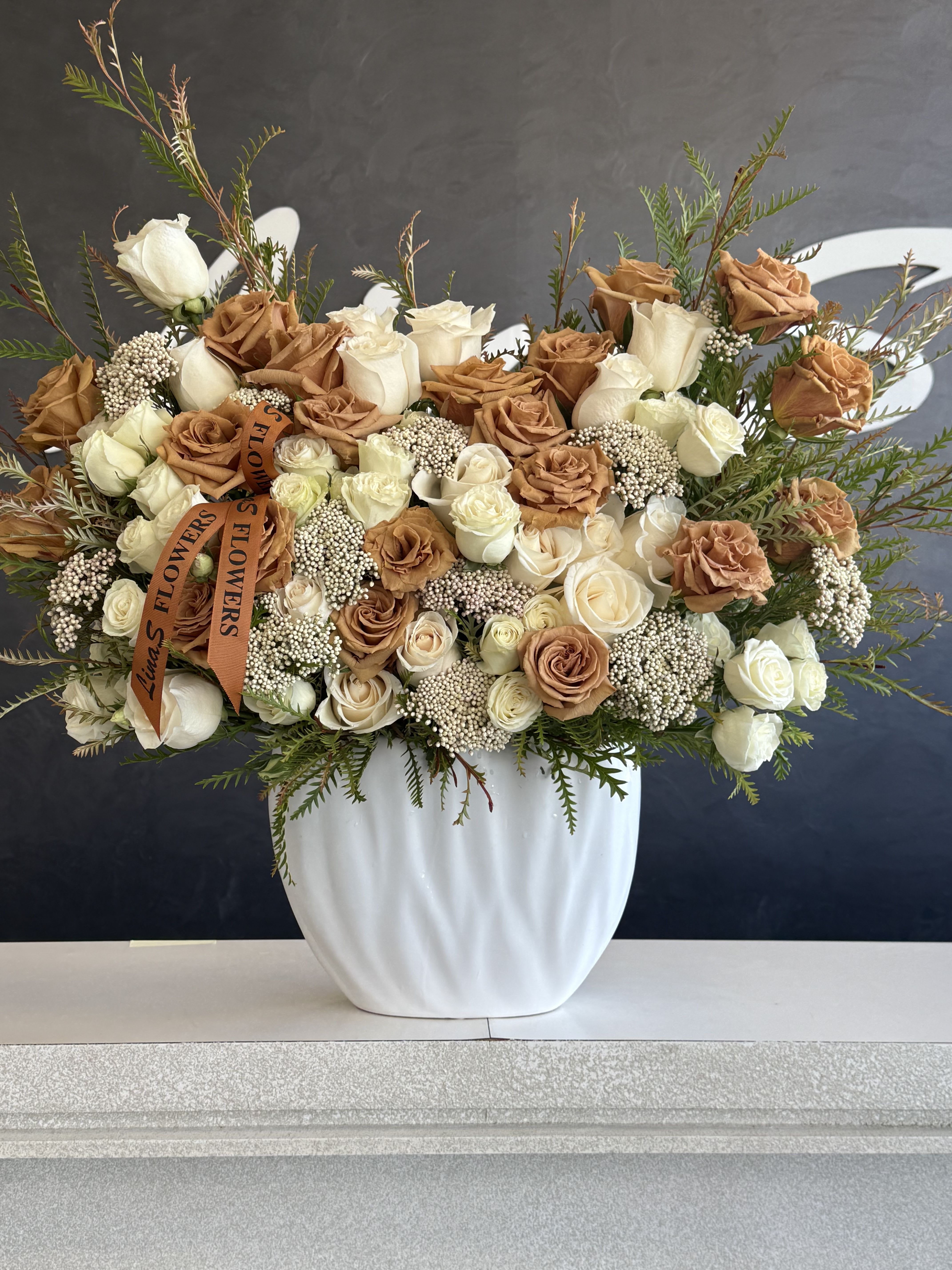 Large rose arrangement in a white vase with tan and white blooms