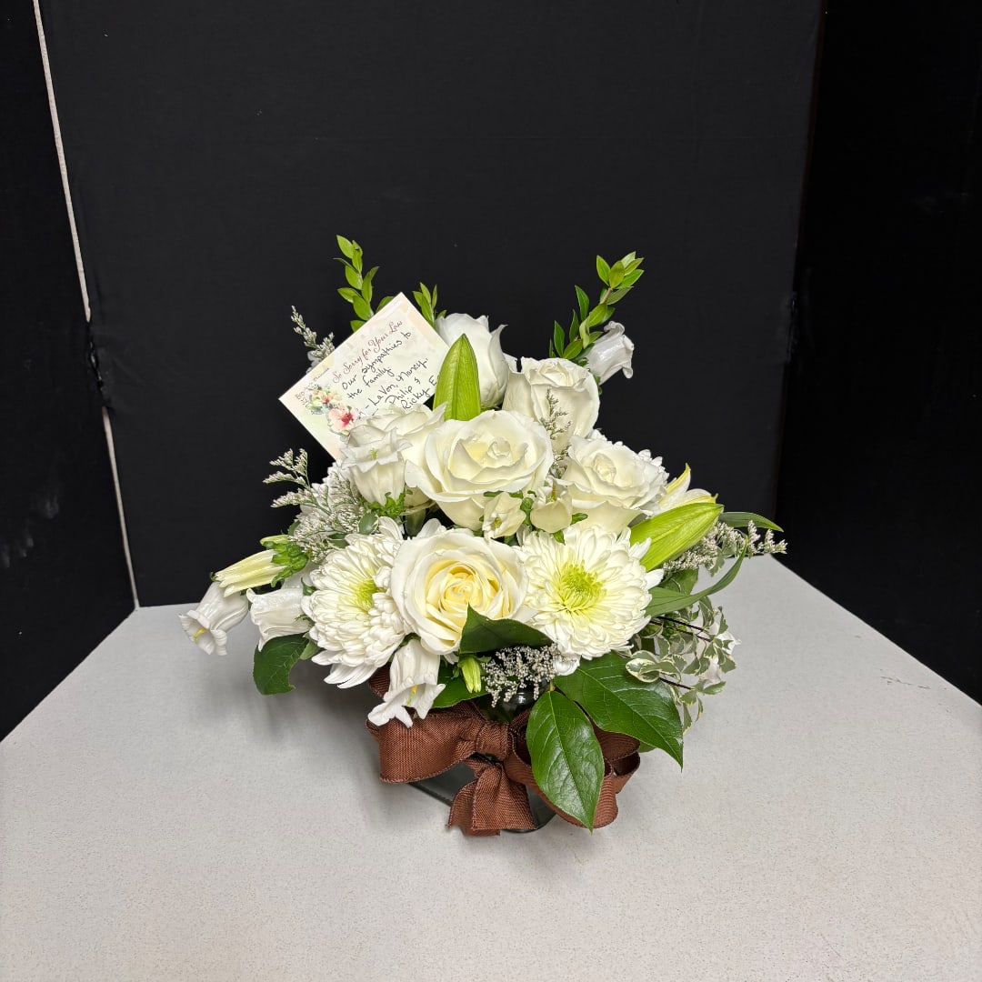 White rose and lily bouquet in a low container with a brown ribbon