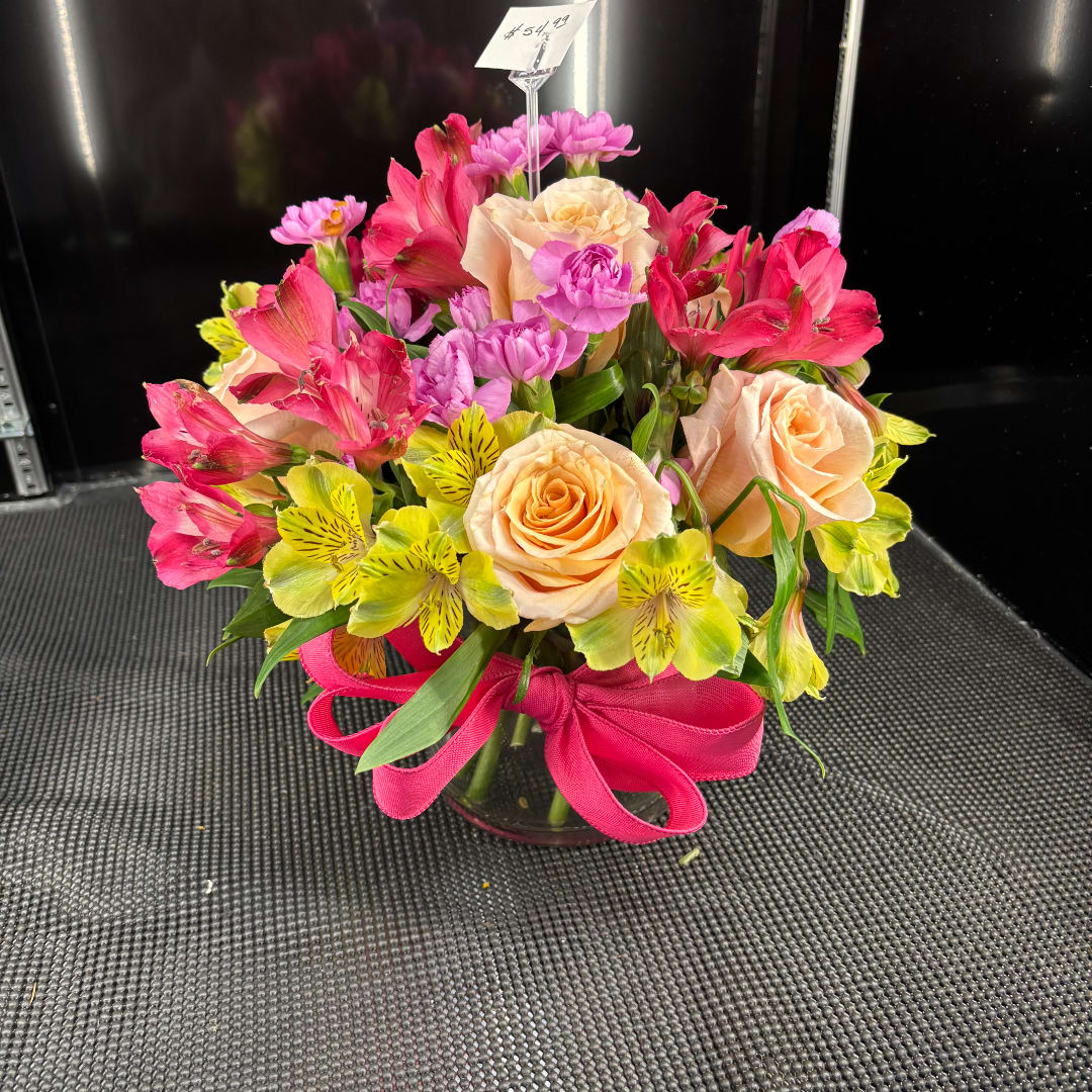 Mixed bouquet of peach roses, pink flowers, and yellow alstroemeria in a glass vase