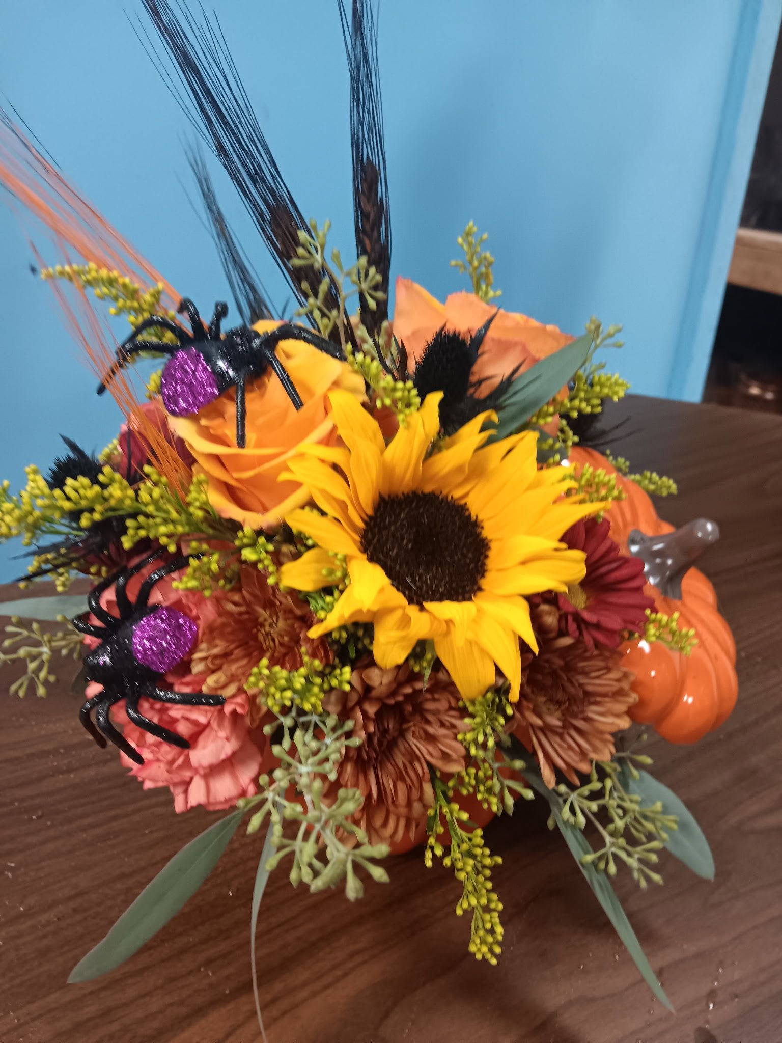 Autumn floral arrangement with sunflowers, roses, and Halloween spider decorations in a pumpkin container