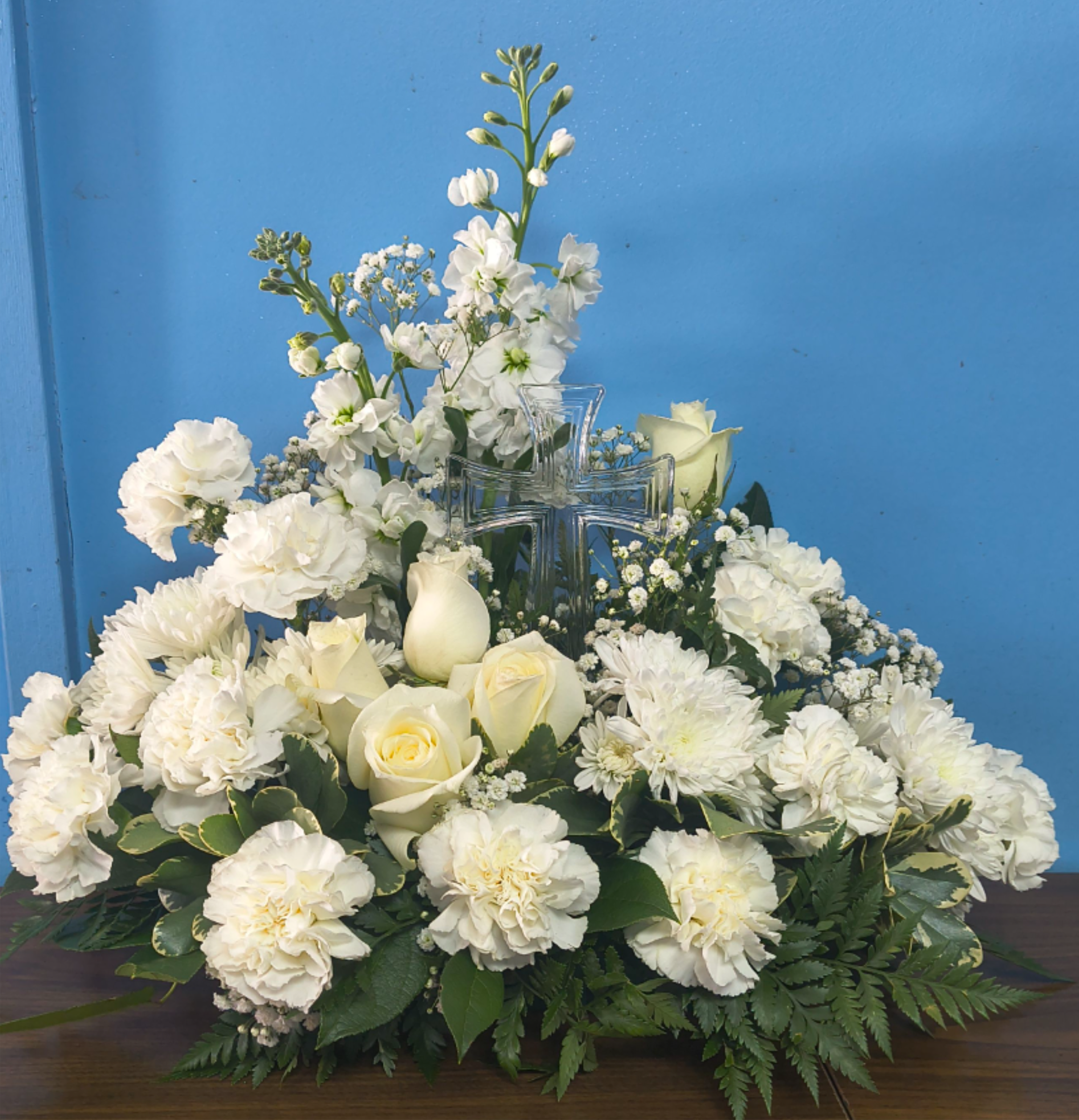 White roses, carnations, and mums arranged around a clear glass cross.