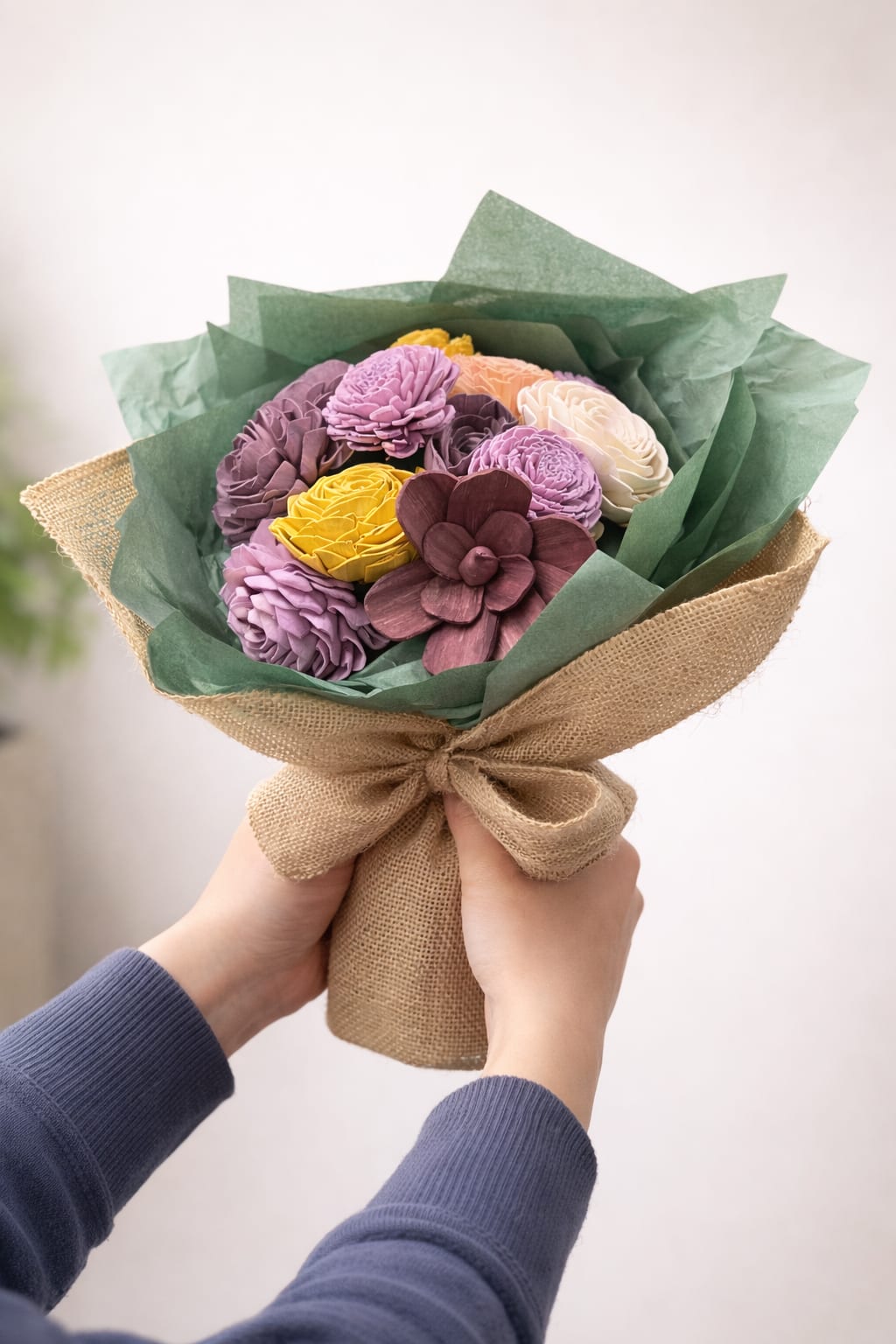 Handheld bouquet of multicolored flowers wrapped in burlap and green paper