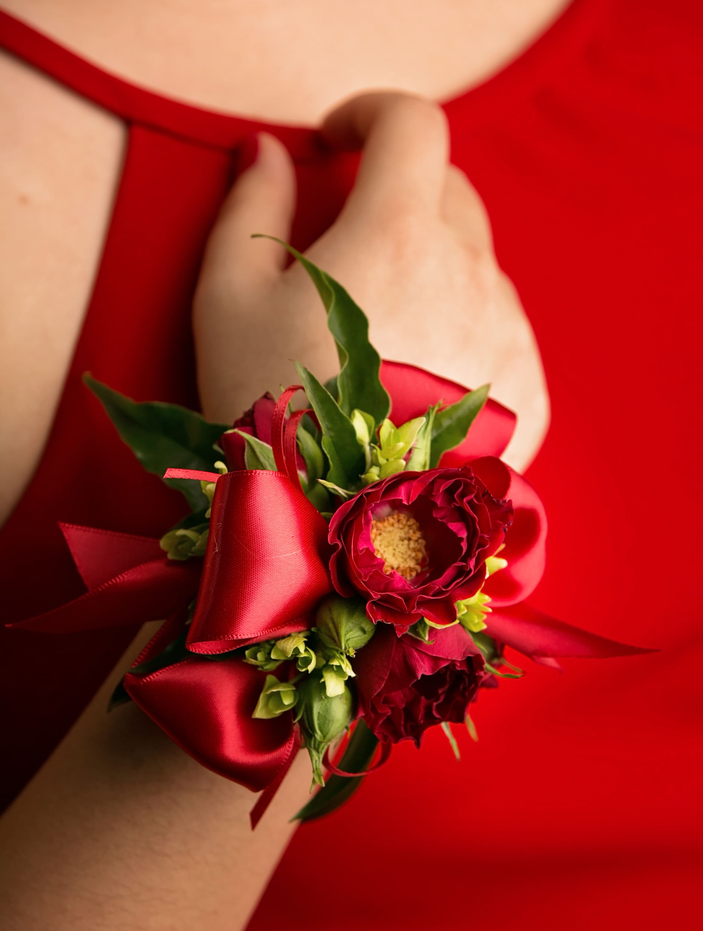 Red wrist corsage with small red flowers and satin ribbon on a wrist in a red dress