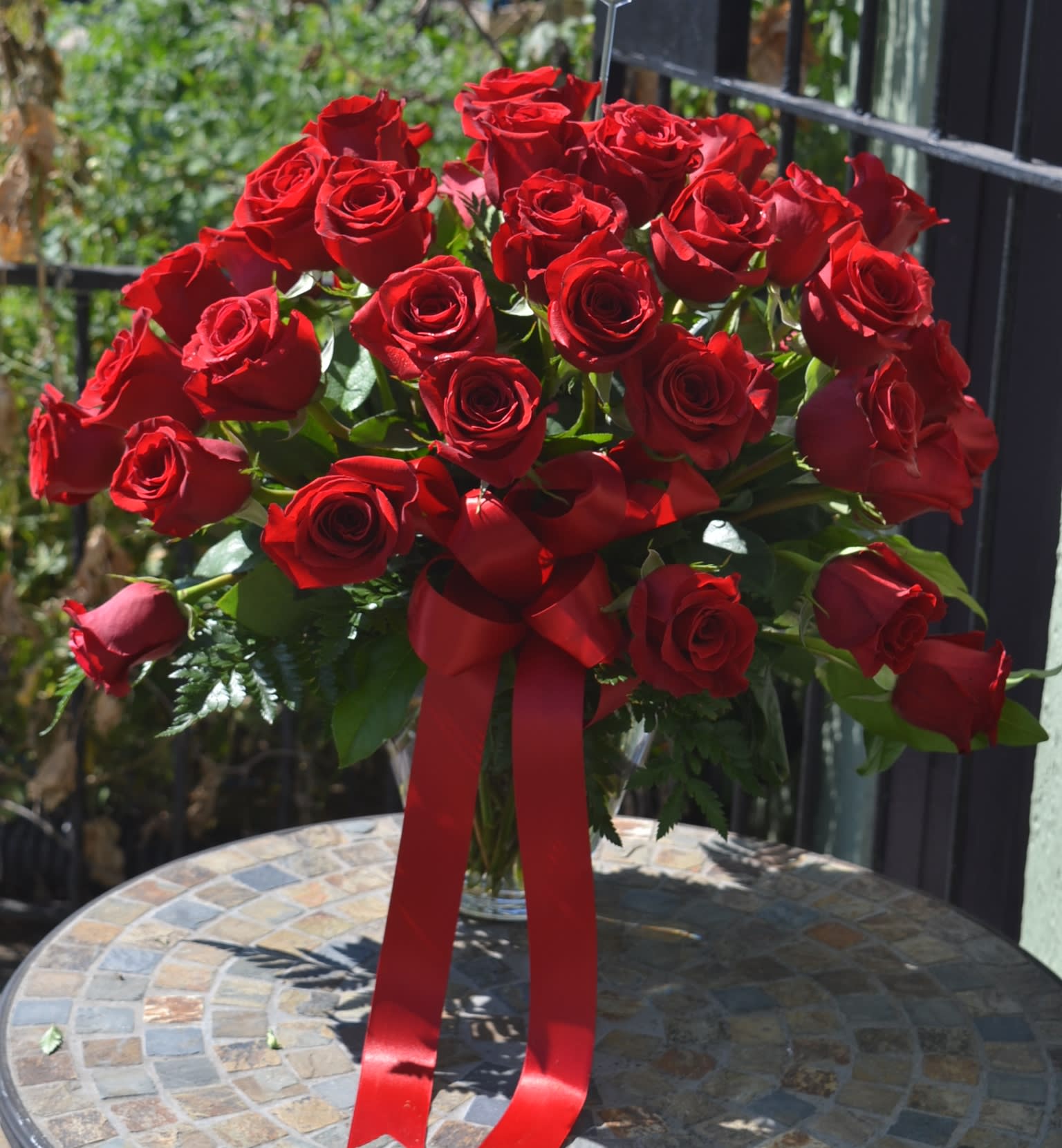 Large bouquet of red roses in a clear vase with a red ribbon bow on a mosaic table