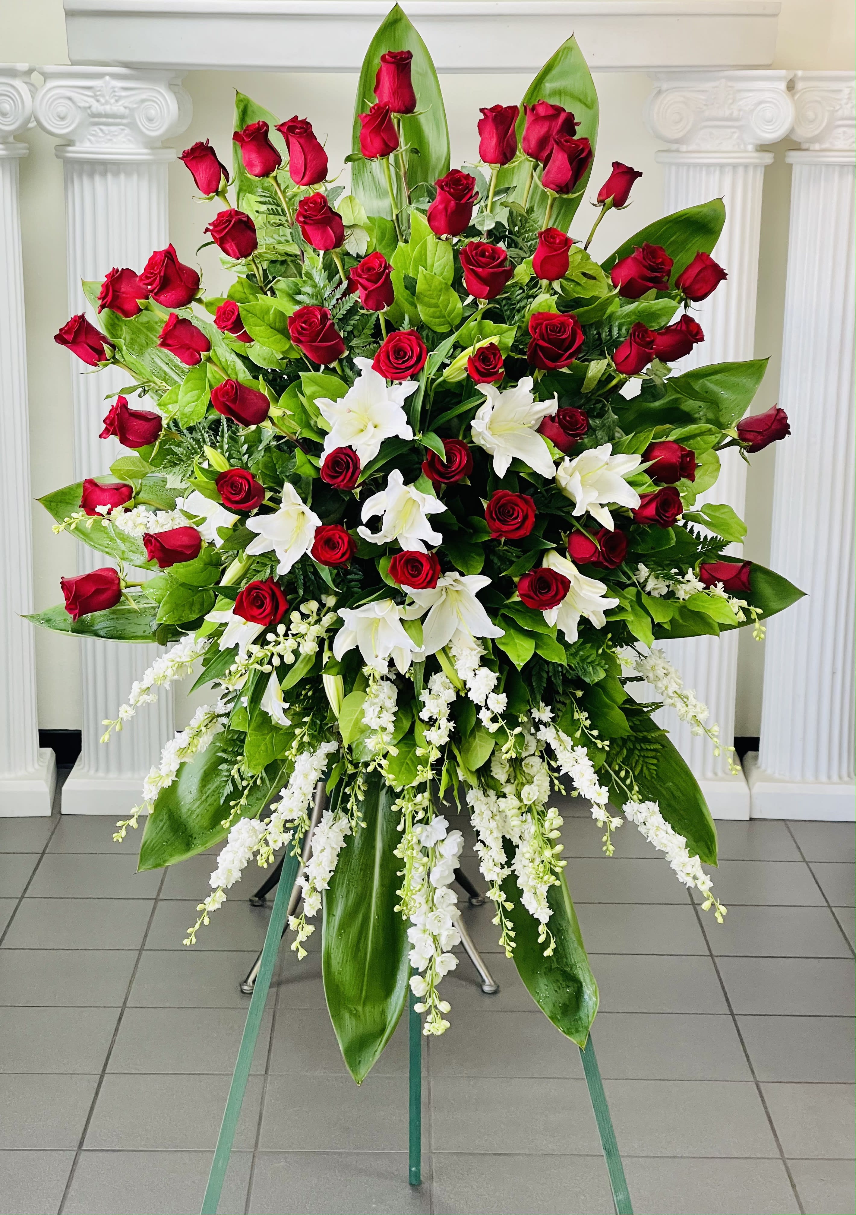 Large standing arrangement of red roses and white lilies with cascading white flowers