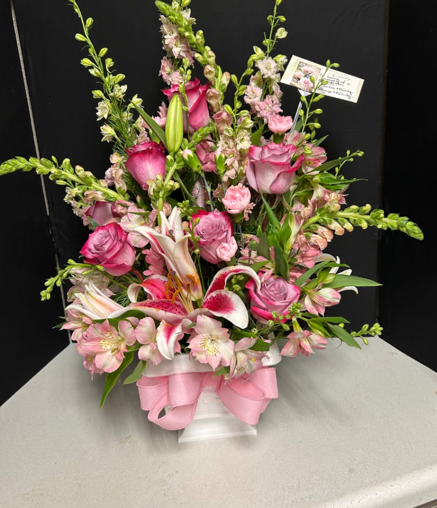Pink and white floral arrangement in a white vase with a pink ribbon