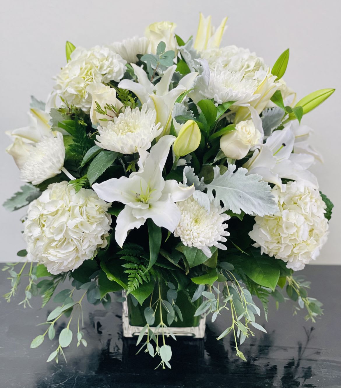 White floral arrangement in a square container with trailing greenery