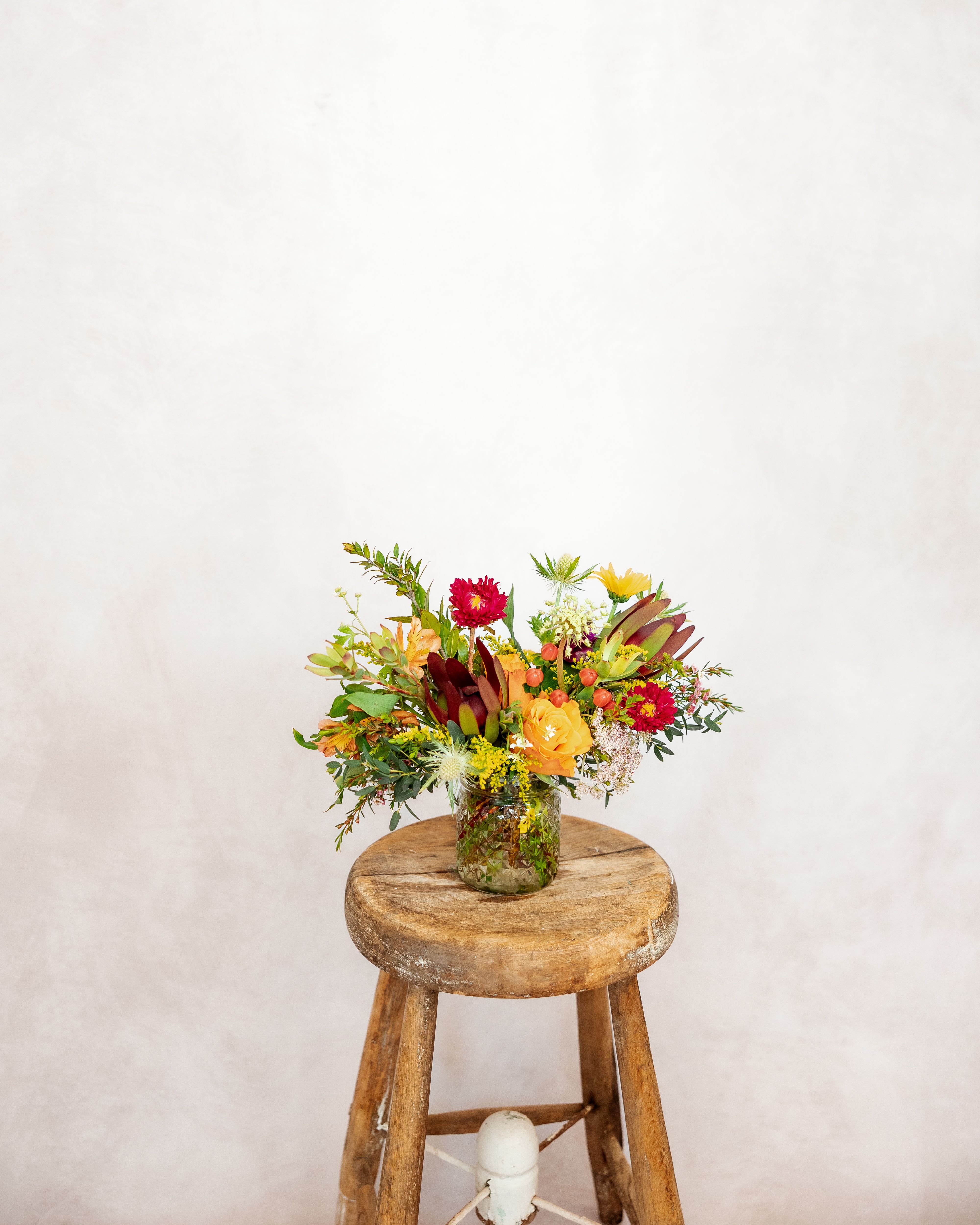Mixed bouquet in a glass jar on a wooden stool