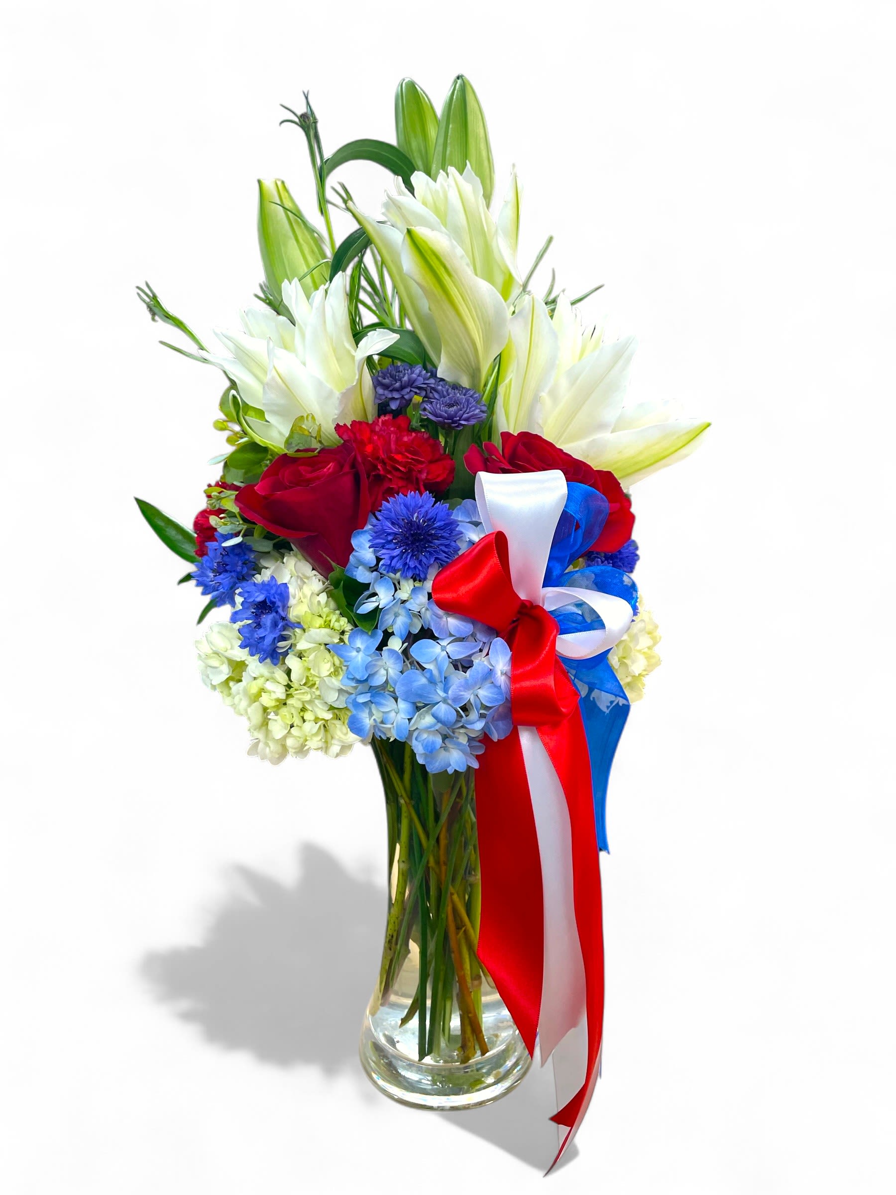Red roses and white lilies in a glass vase with a red, white, and blue ribbon