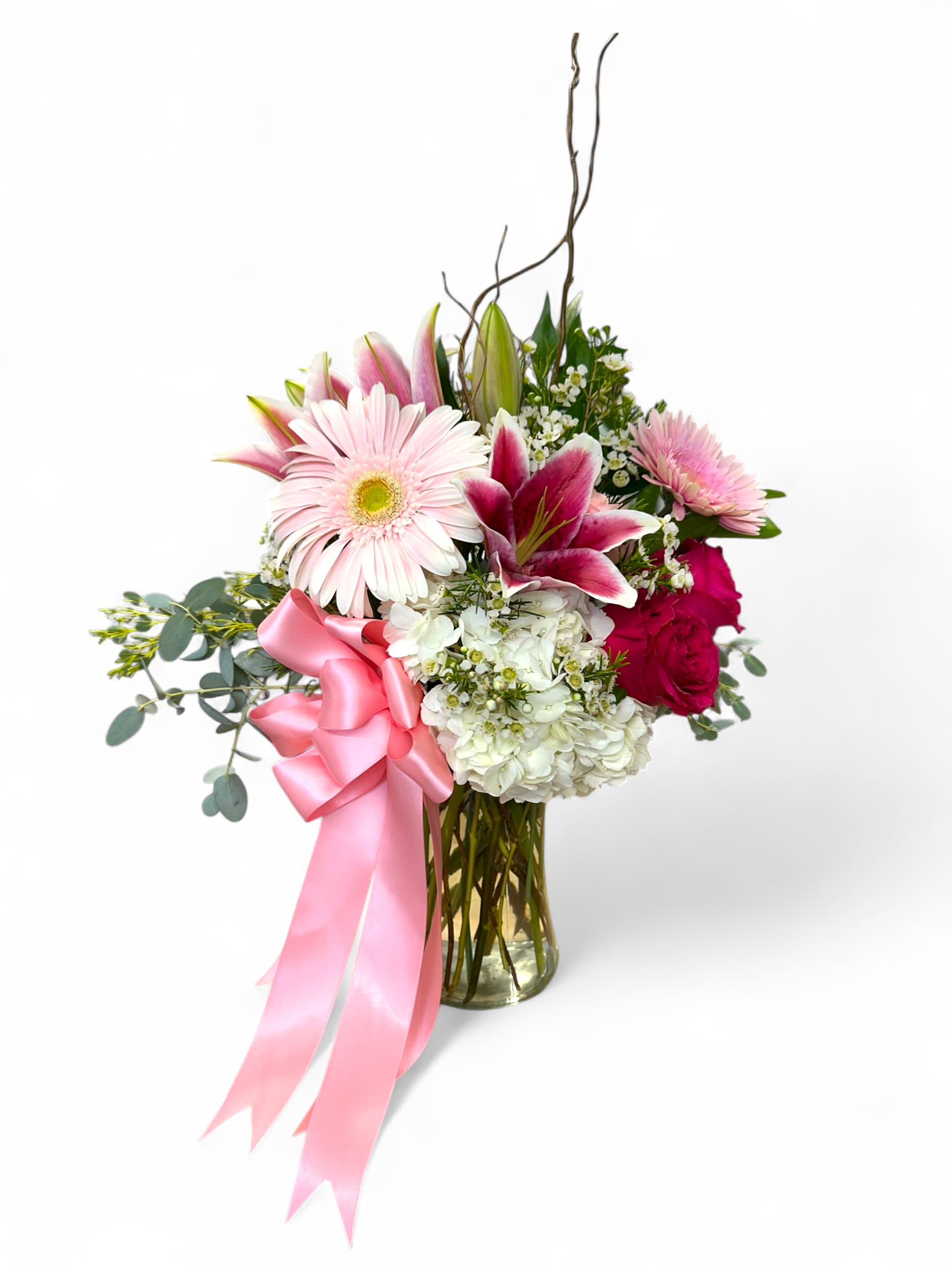 Pink and white floral arrangement in a glass vase with a pink ribbon