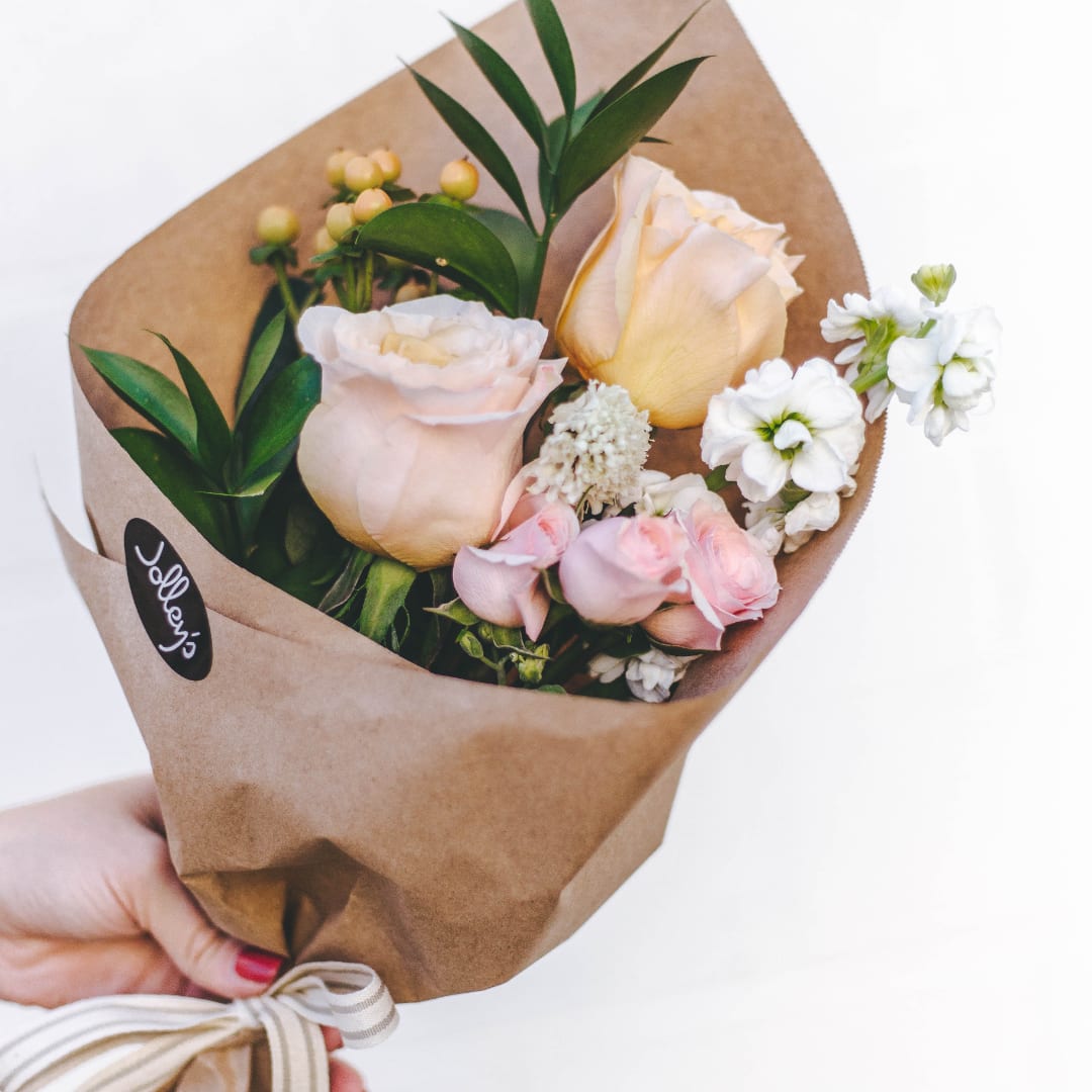 Handheld bouquet of pale roses and white flowers wrapped in brown paper