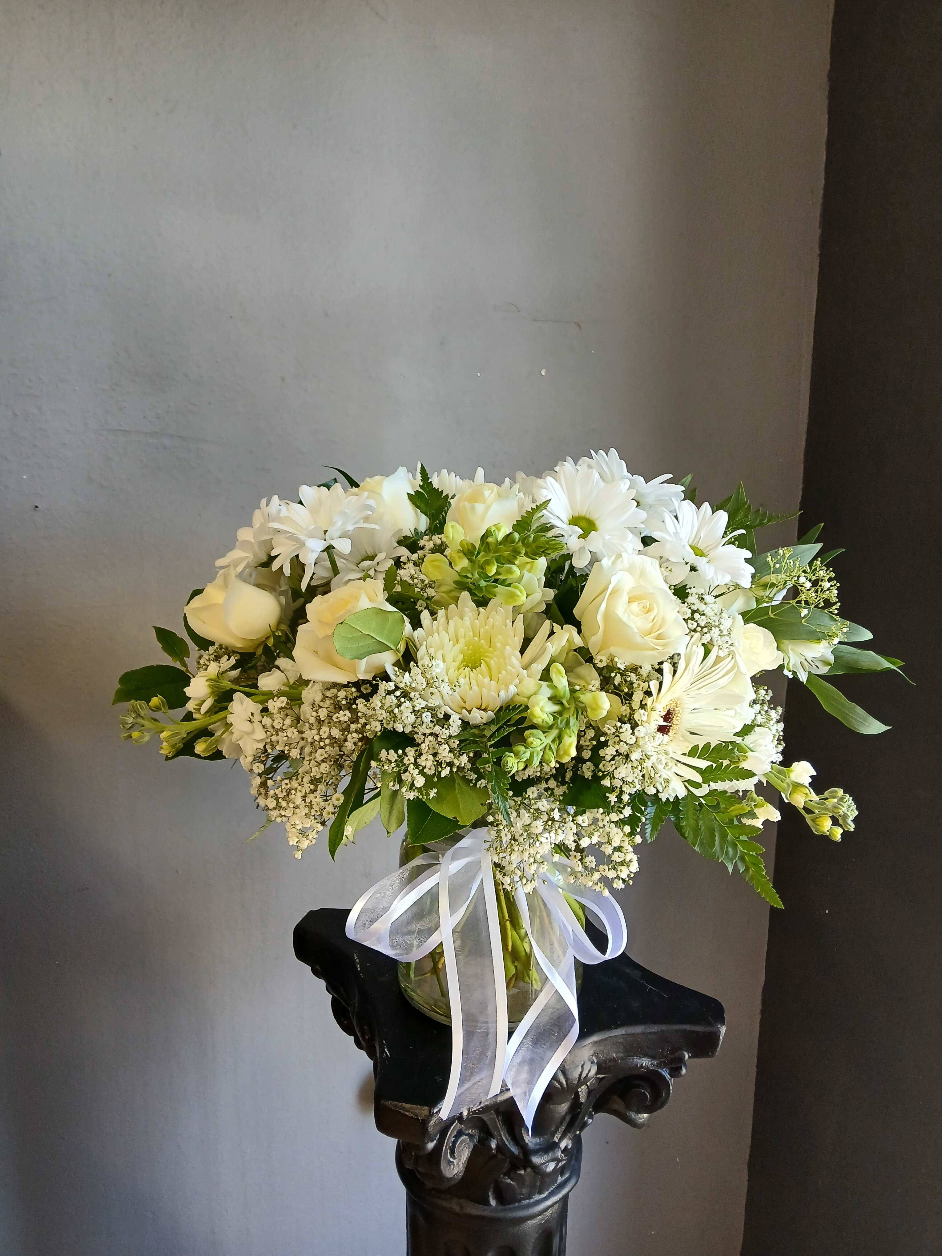White rose and daisy bouquet in a glass vase with a white ribbon