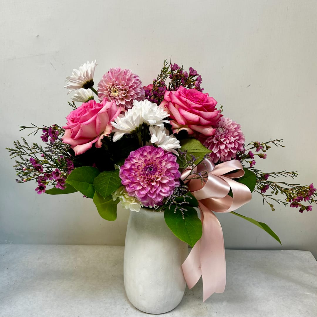 Pink roses and mixed blooms in a white vase with a pink ribbon
