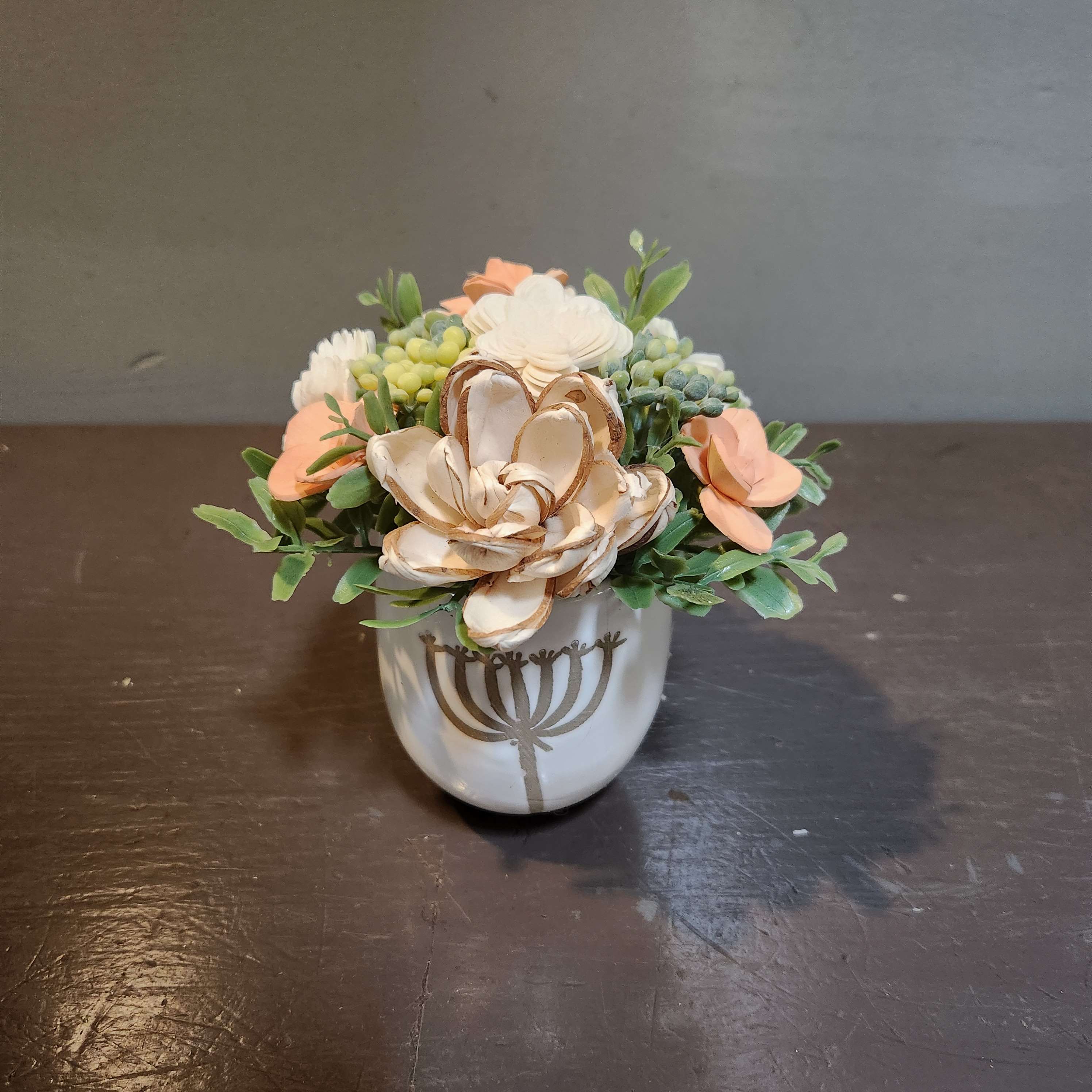 Small floral arrangement in a white ceramic pot with peach and cream blooms