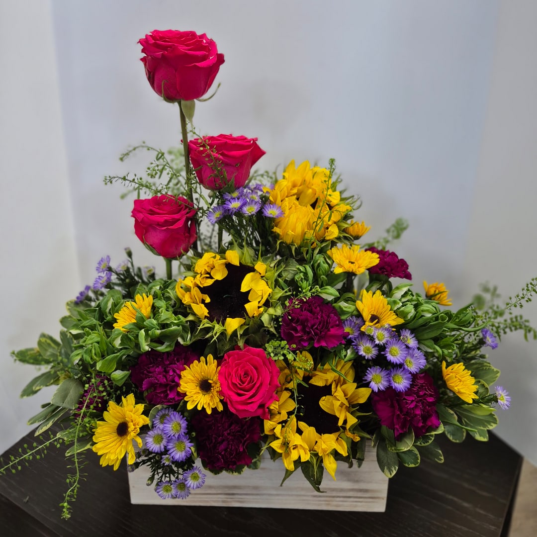 Mixed floral arrangement with pink roses, yellow sunflowers, and purple daisies in a wooden box