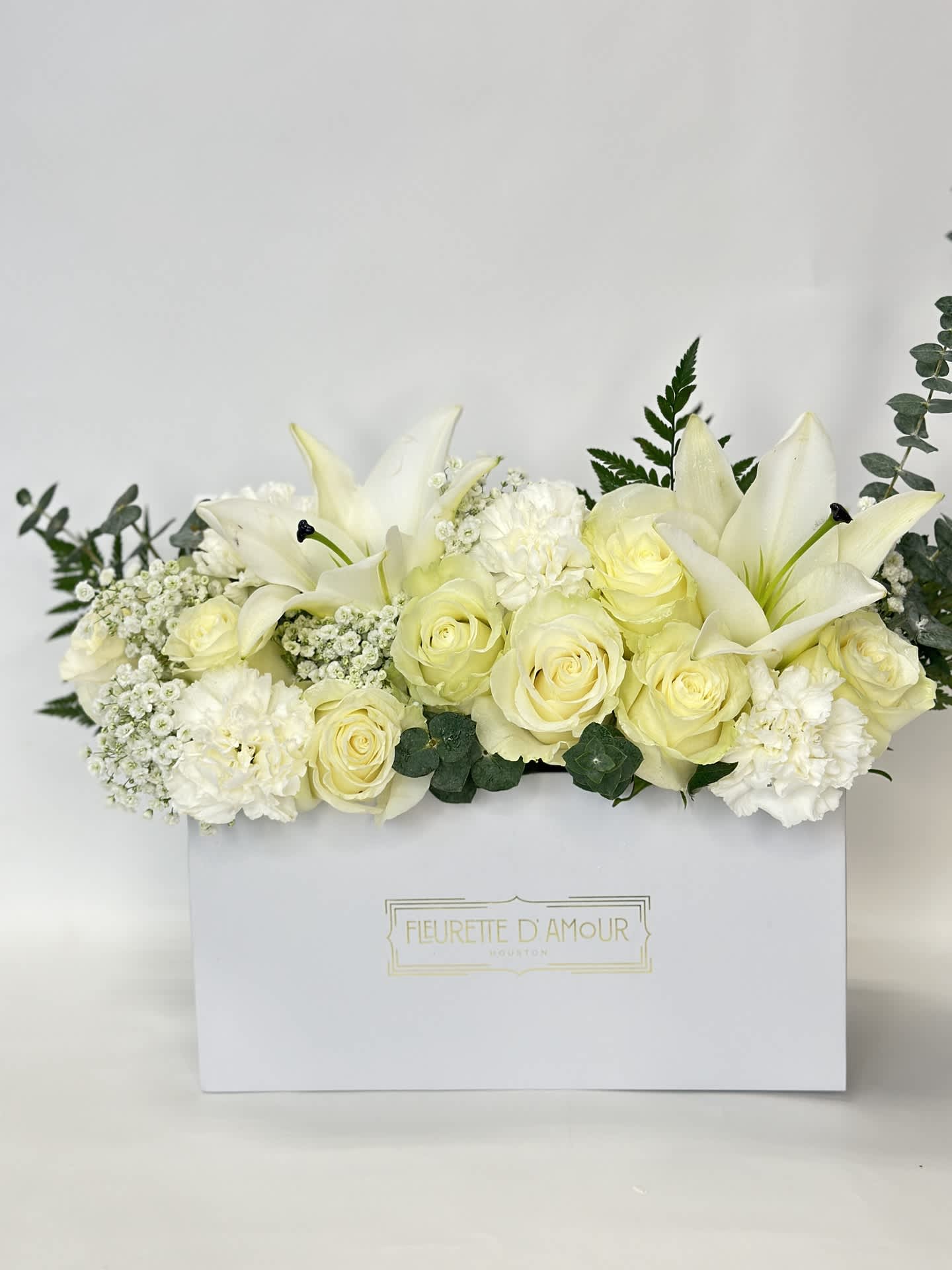 White roses and lilies arranged in a white gift box