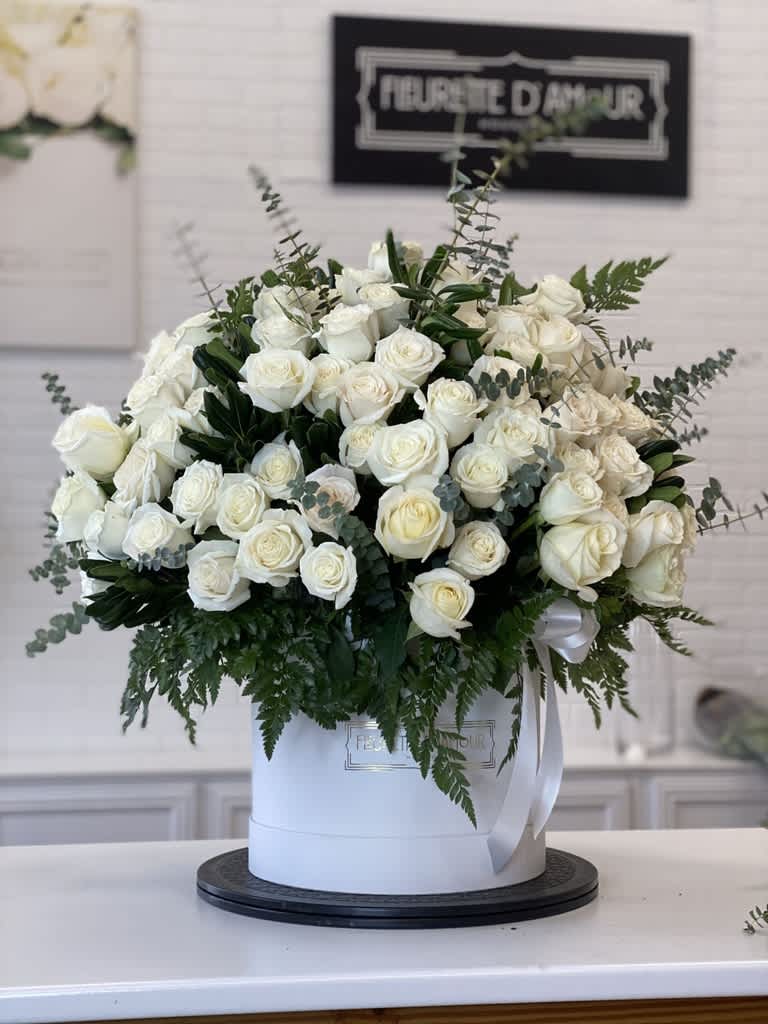 Large white rose arrangement in a round white box with greenery