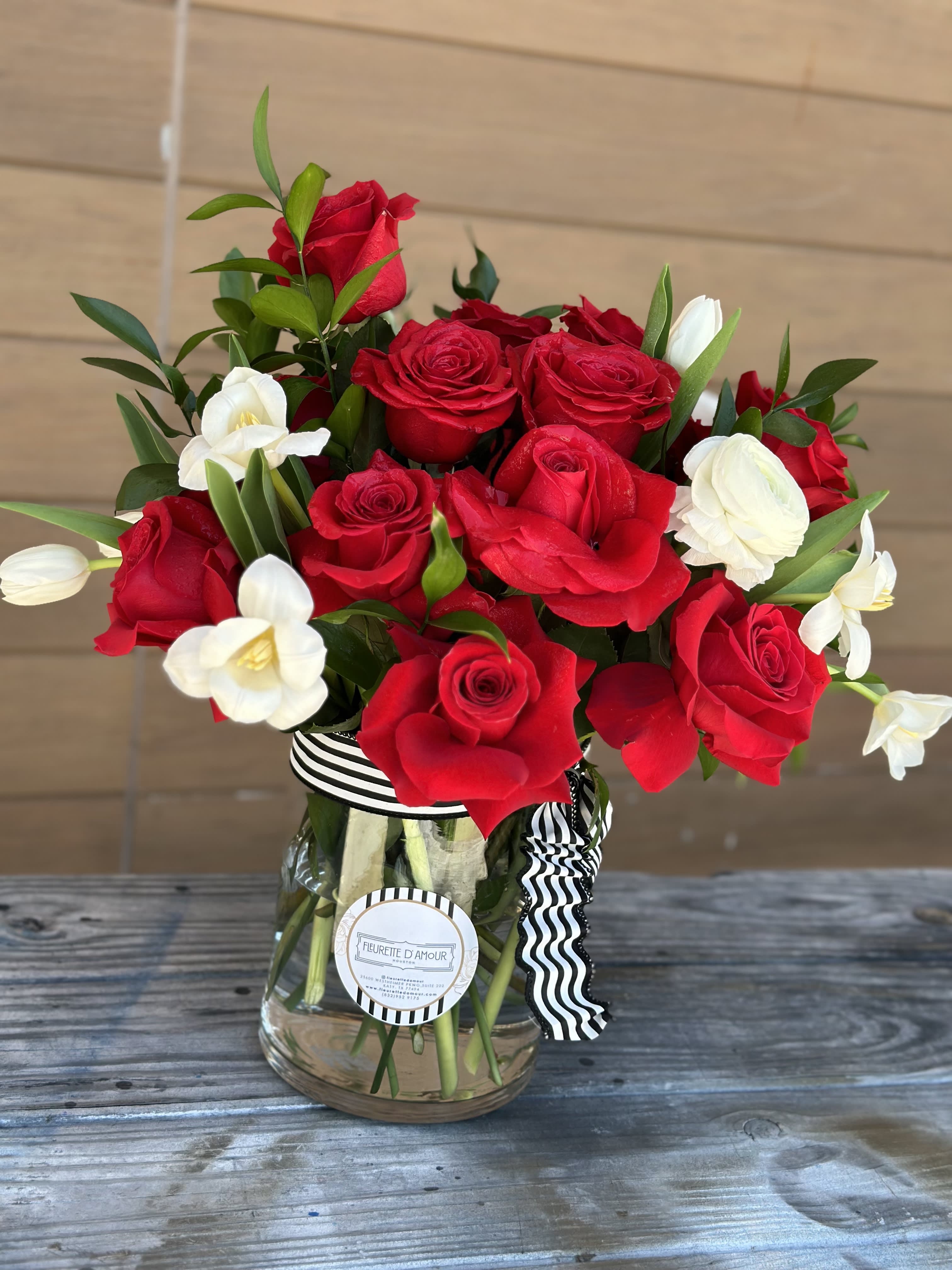 Red roses and white flowers arranged in a glass vase with a striped ribbon.