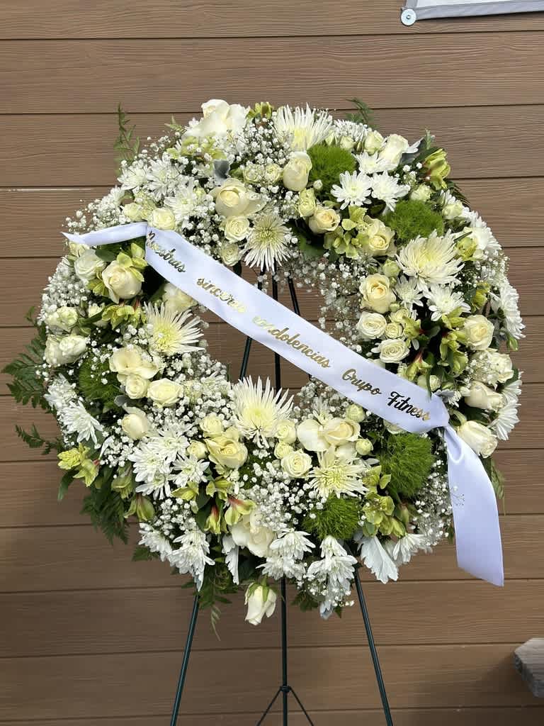 White floral wreath on an easel with a ribbon across the center