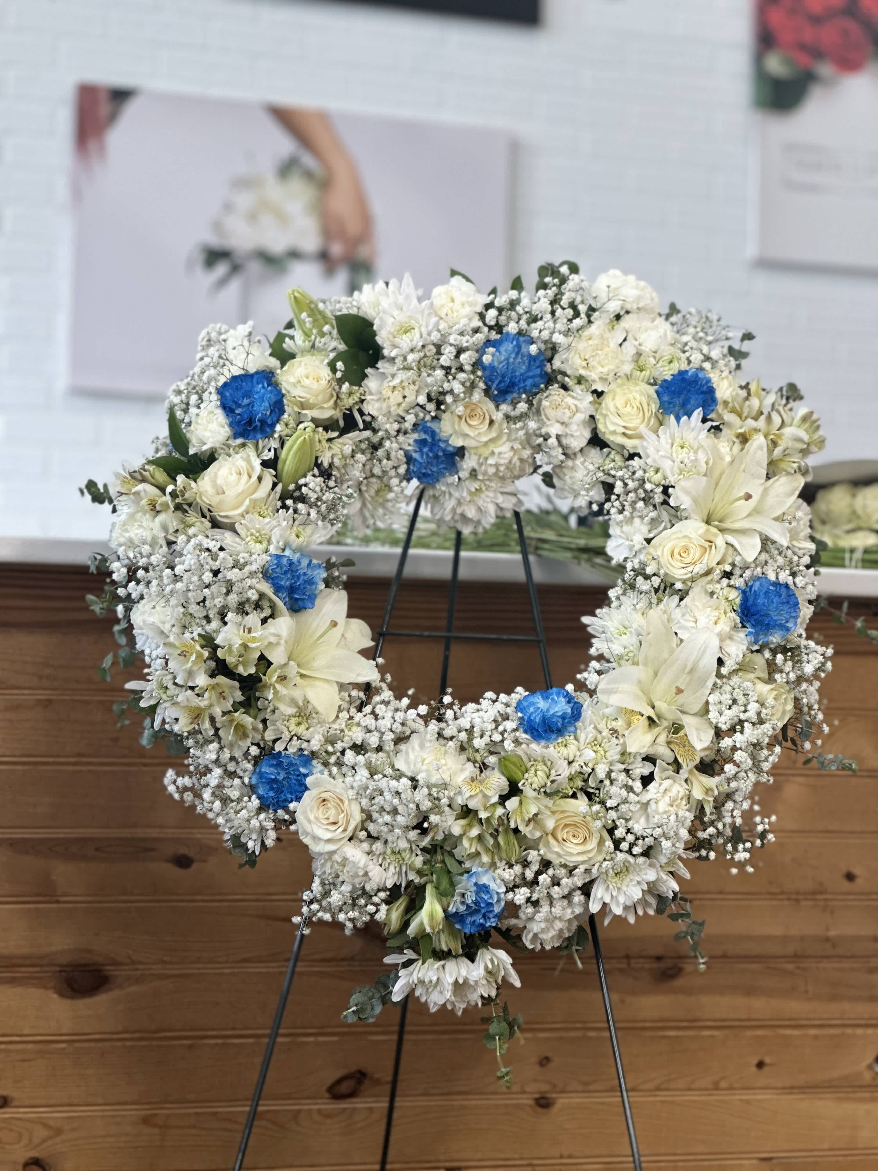 White floral wreath with blue accents on a stand