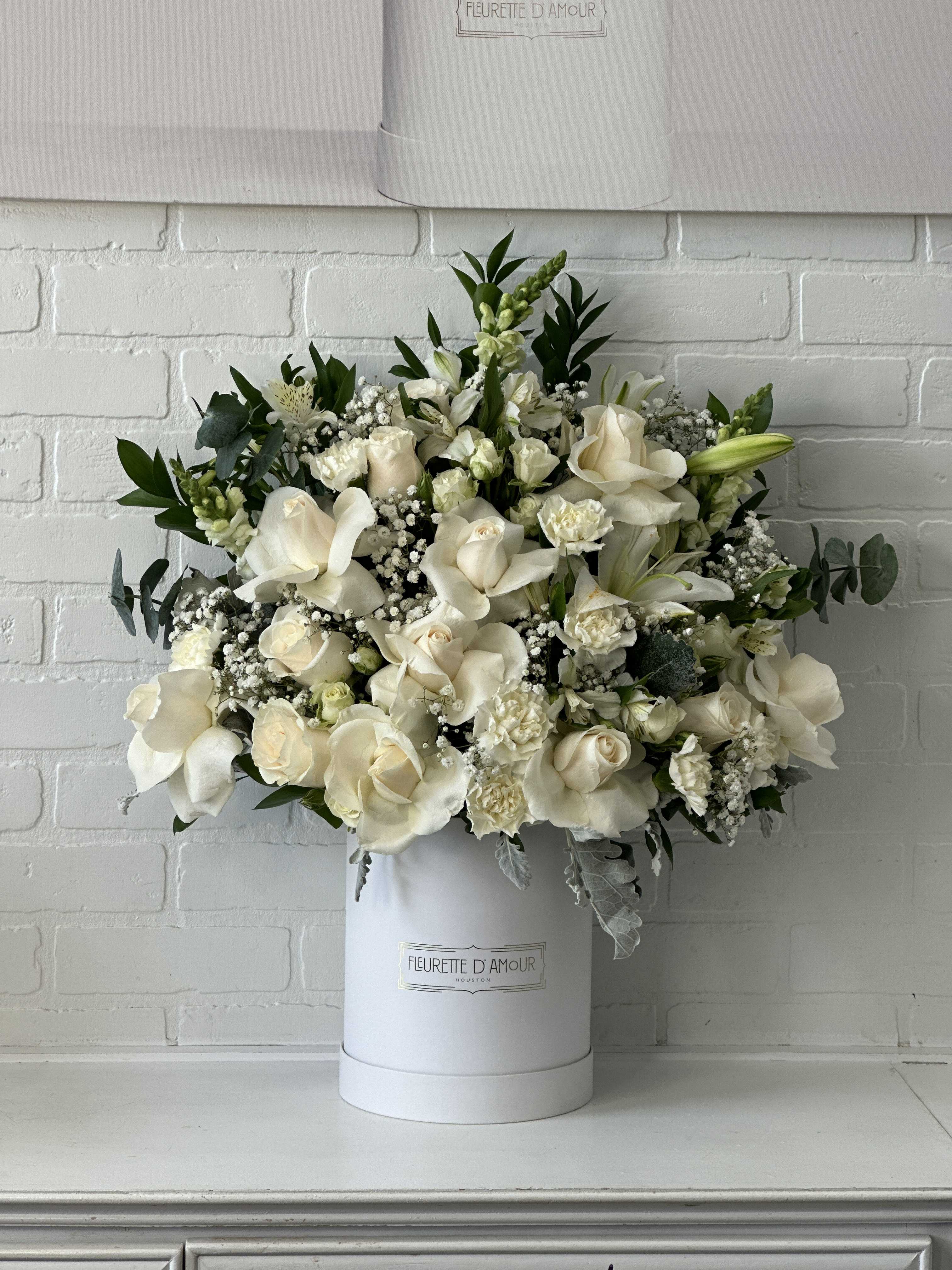 White floral arrangement in a tall white hatbox with roses and lilies