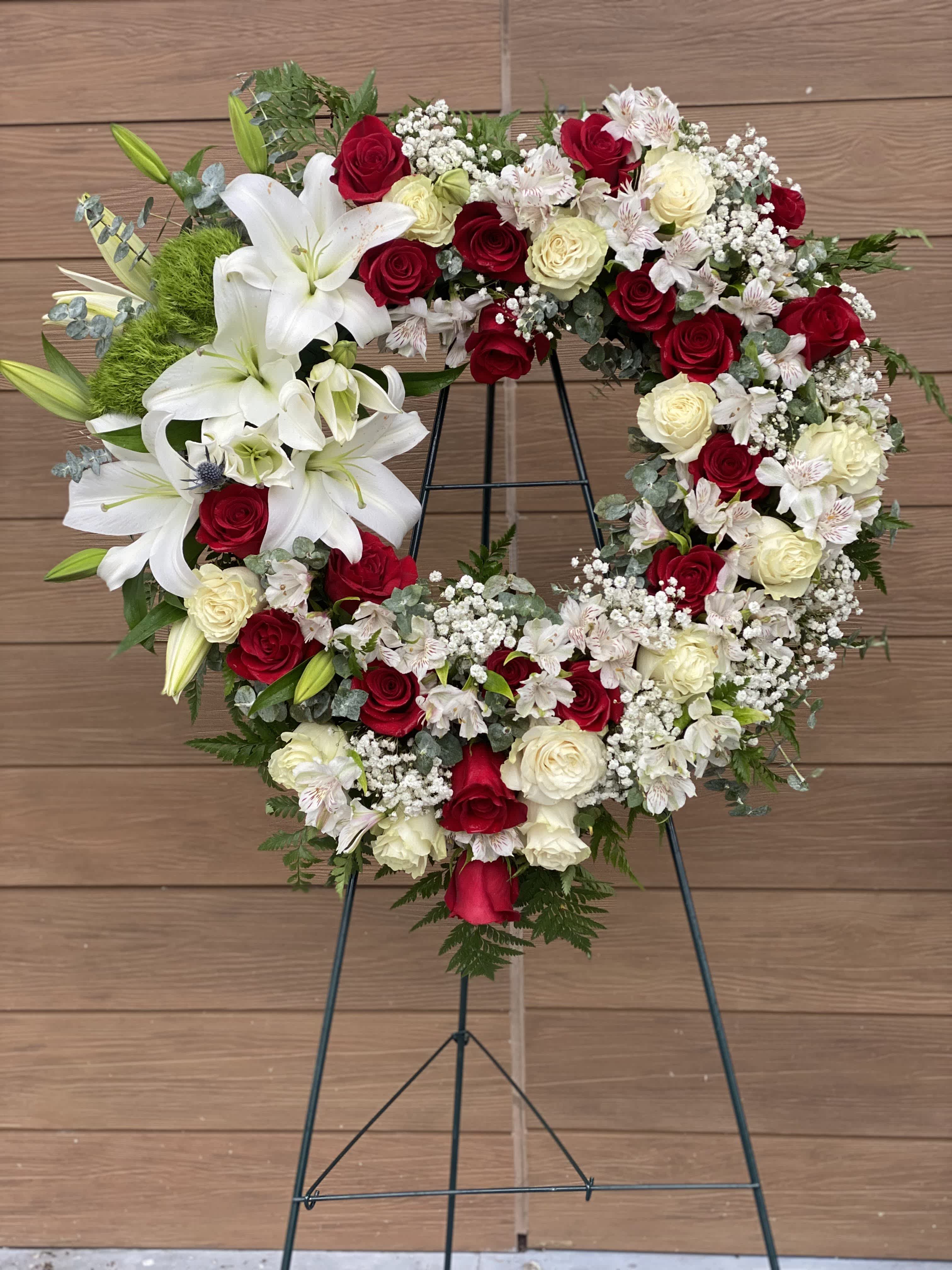Heart-shaped floral wreath with red and white roses and lilies on a stand