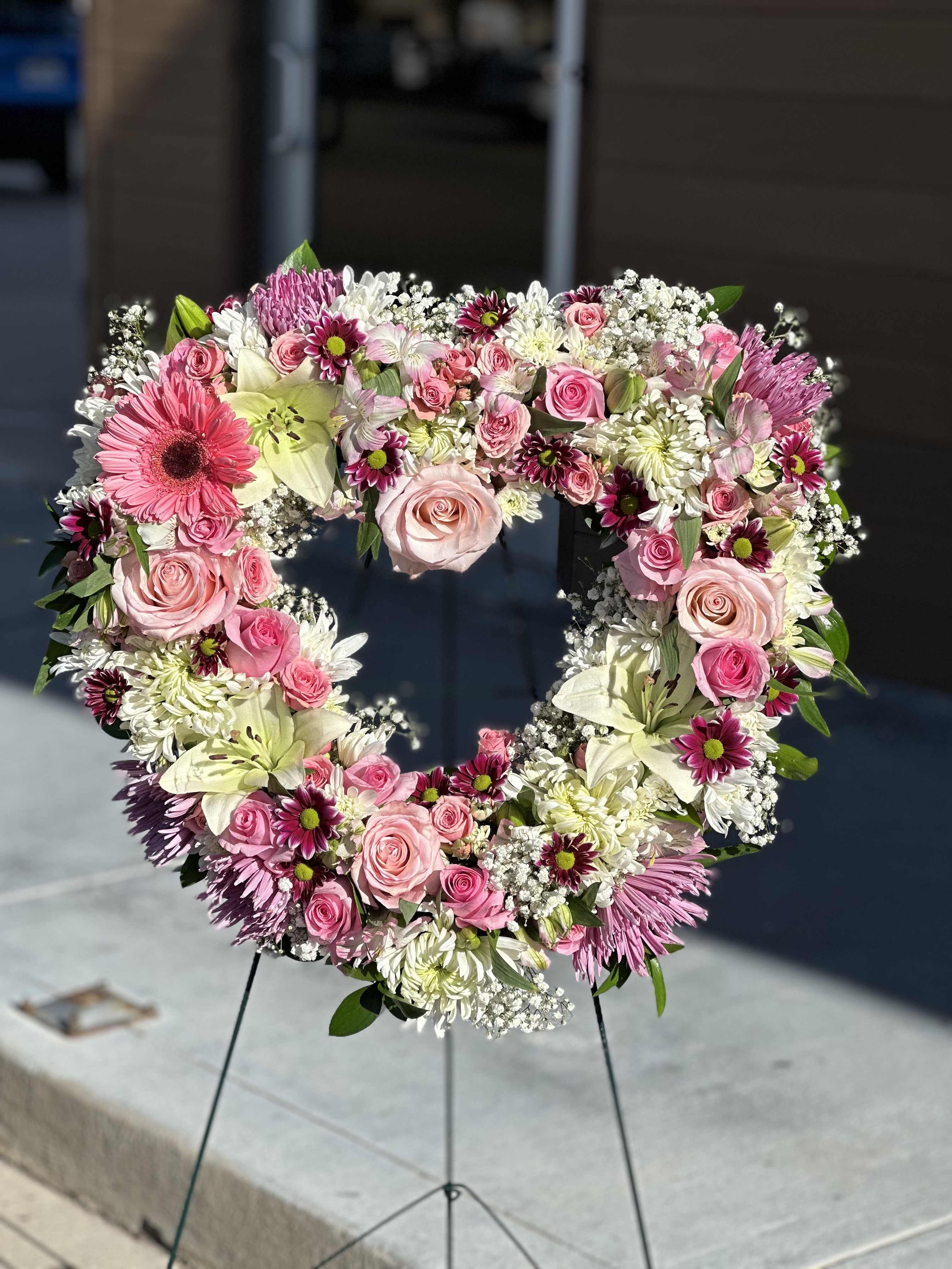 Heart-shaped floral wreath with pink roses and white lilies on a stand