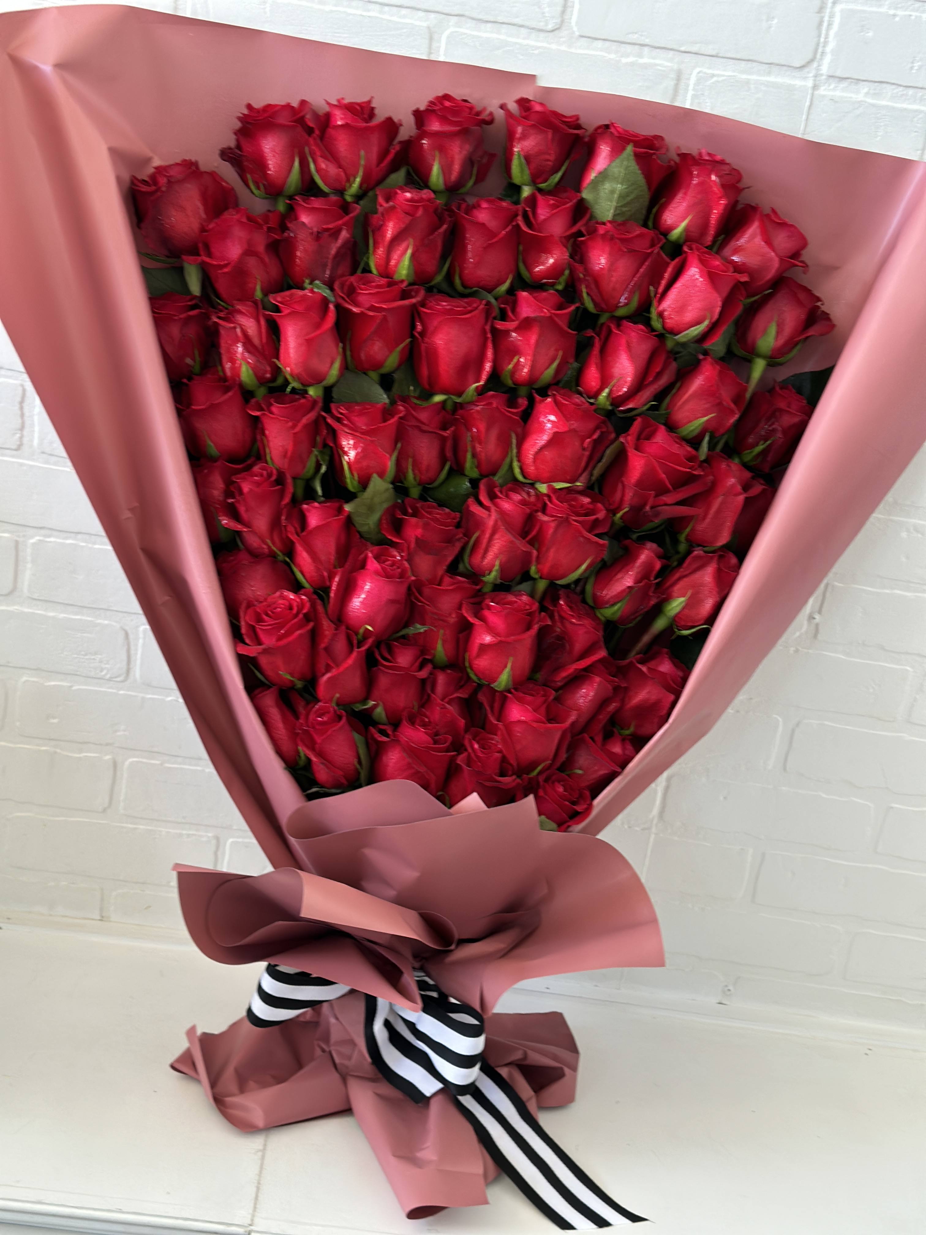 Large bouquet of red roses wrapped in pink paper with a striped ribbon