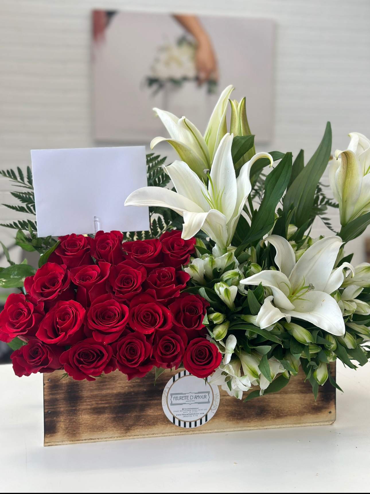 Red roses and white lilies arranged in a wooden box with a blank card