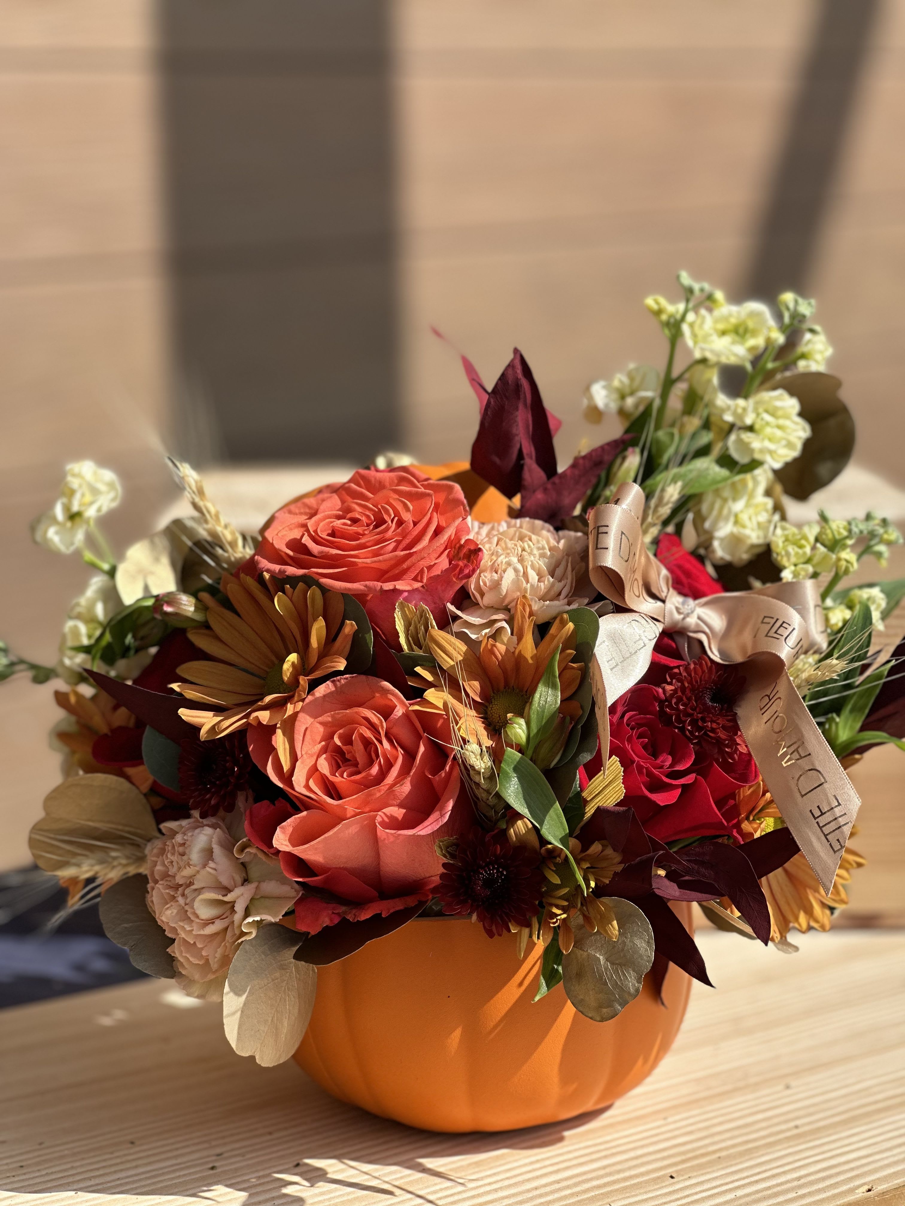 Orange pumpkin-shaped container with mixed autumn flowers and ribbon
