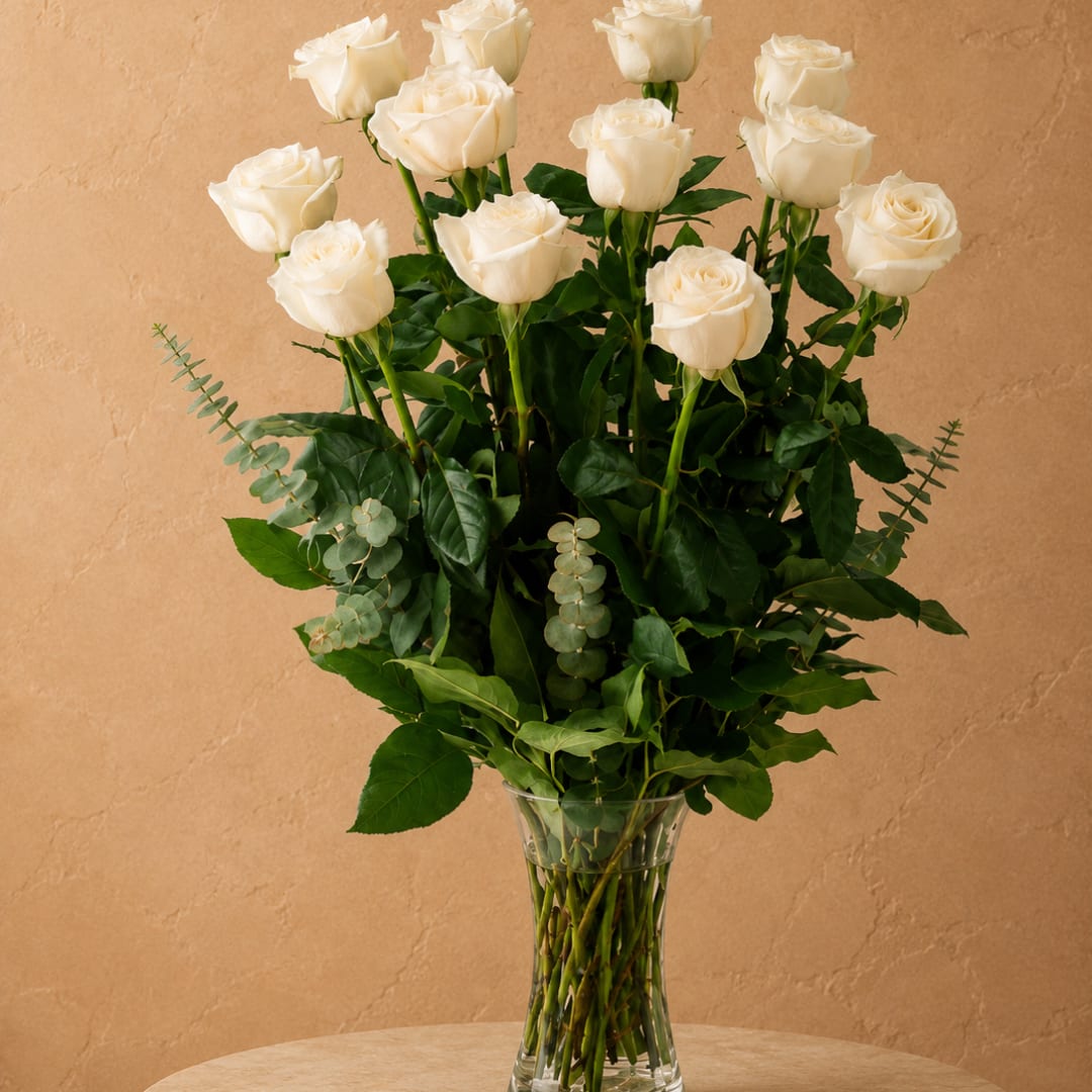 White roses arranged in a clear glass vase with greenery