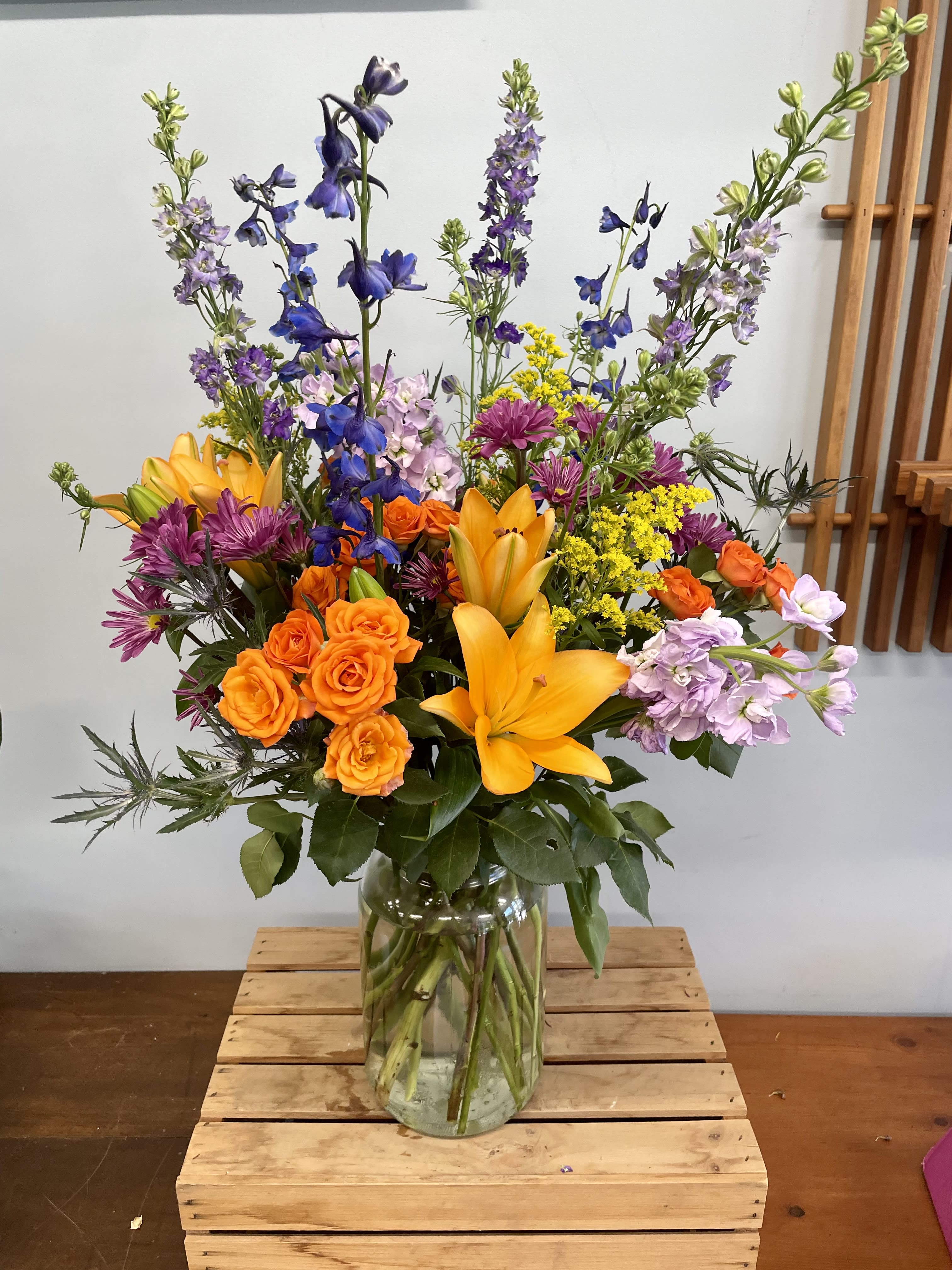 Colorful mixed bouquet in a clear glass vase with orange roses and yellow lilies