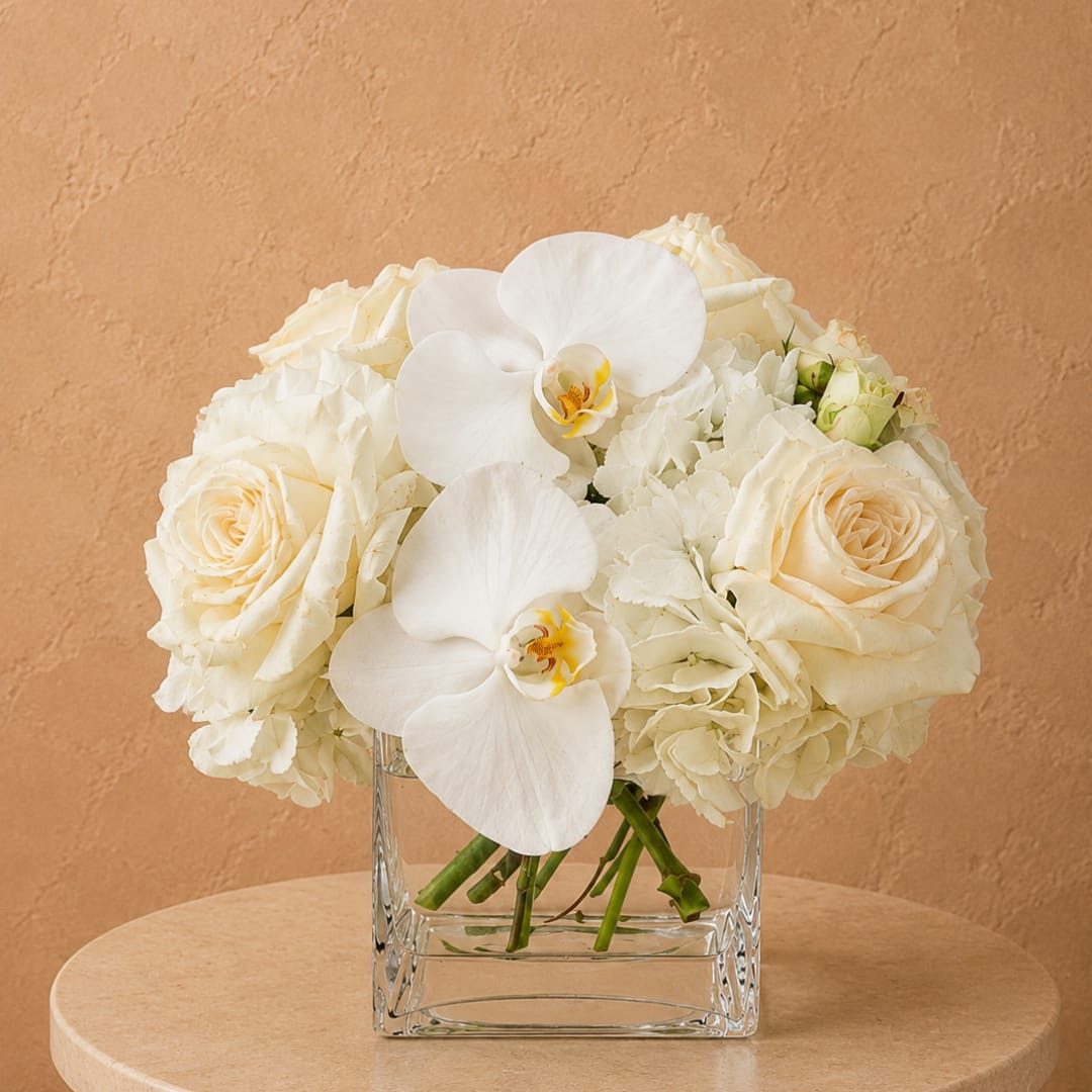 White roses and orchids arranged in a clear square vase