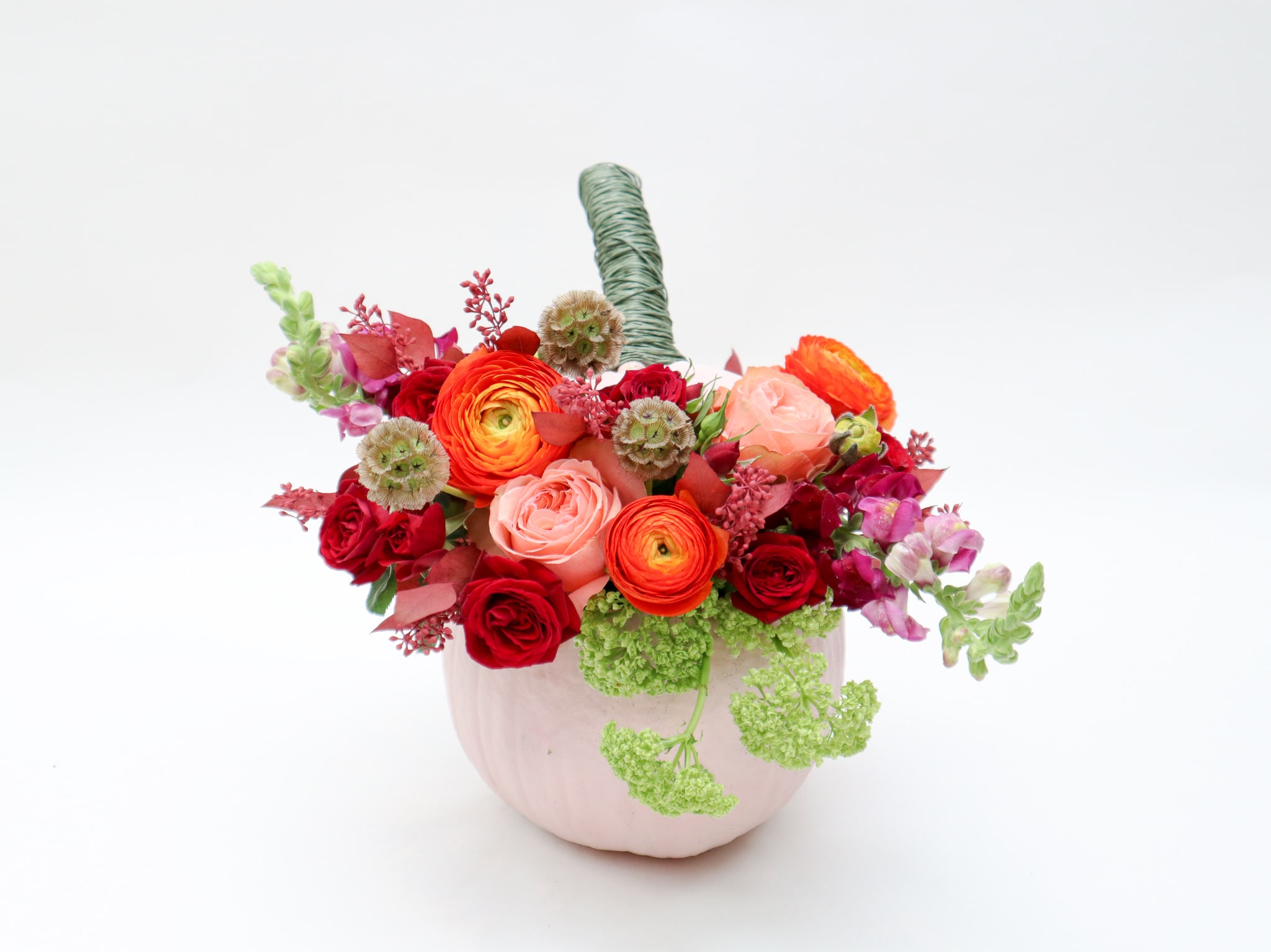 Mixed bouquet of red, pink, and orange flowers in a pale pink vase
