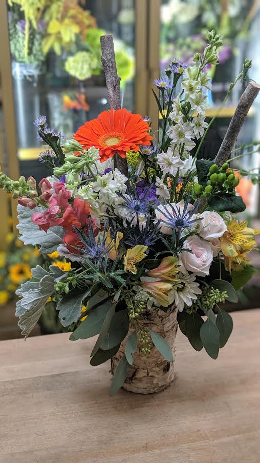 Mixed bouquet in a birch bark vase with orange, white, pink, and blue flowers