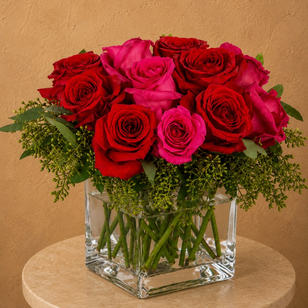 Red and pink roses arranged in a clear glass cube vase