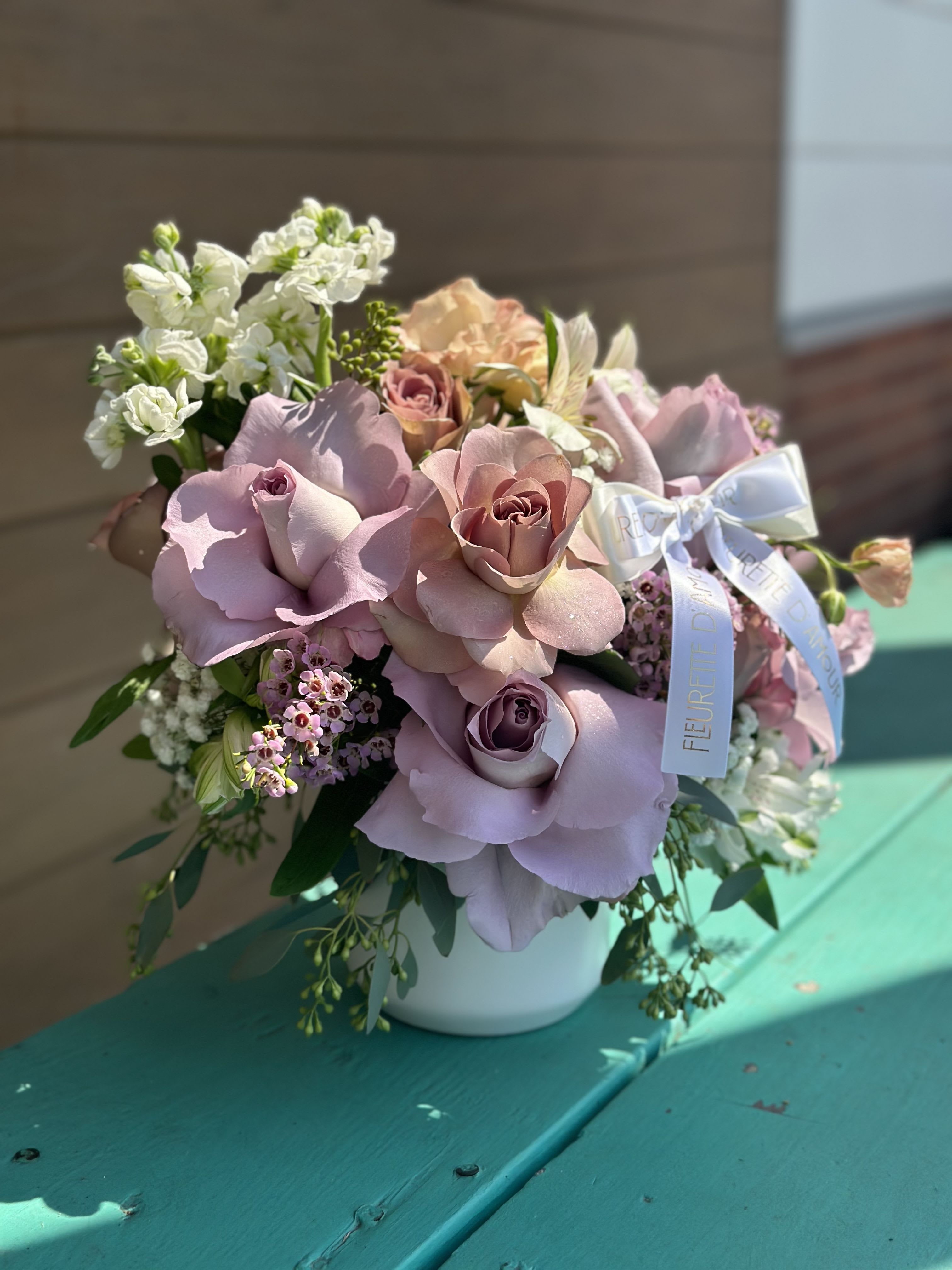 Pink and lavender rose bouquet in a white vase with a ribbon