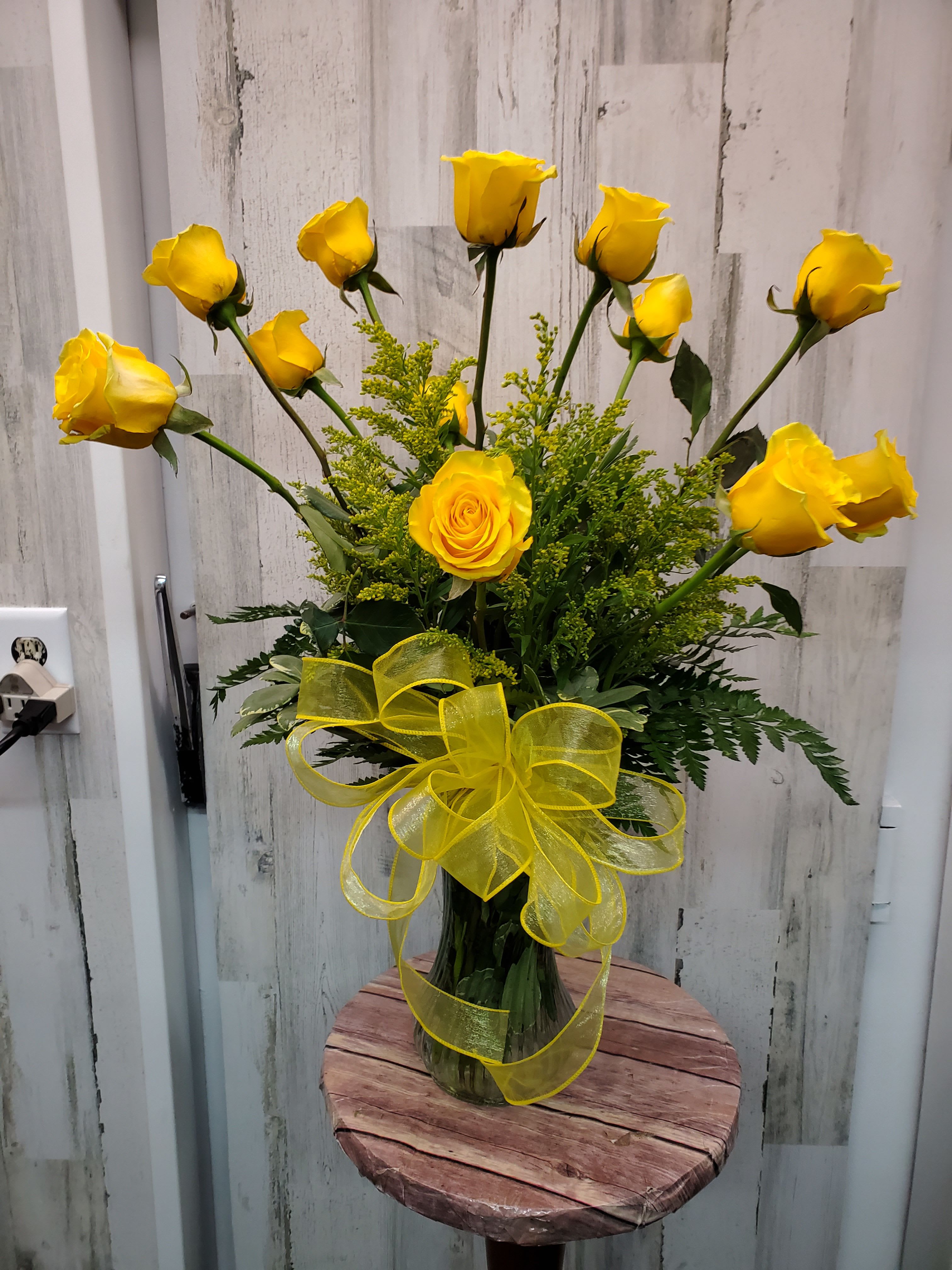 Yellow roses arranged in a clear glass vase with a yellow ribbon.