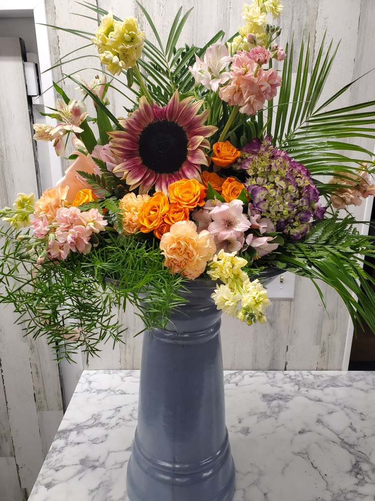 Mixed bouquet in a tall blue vase with sunflowers, roses, and lilies