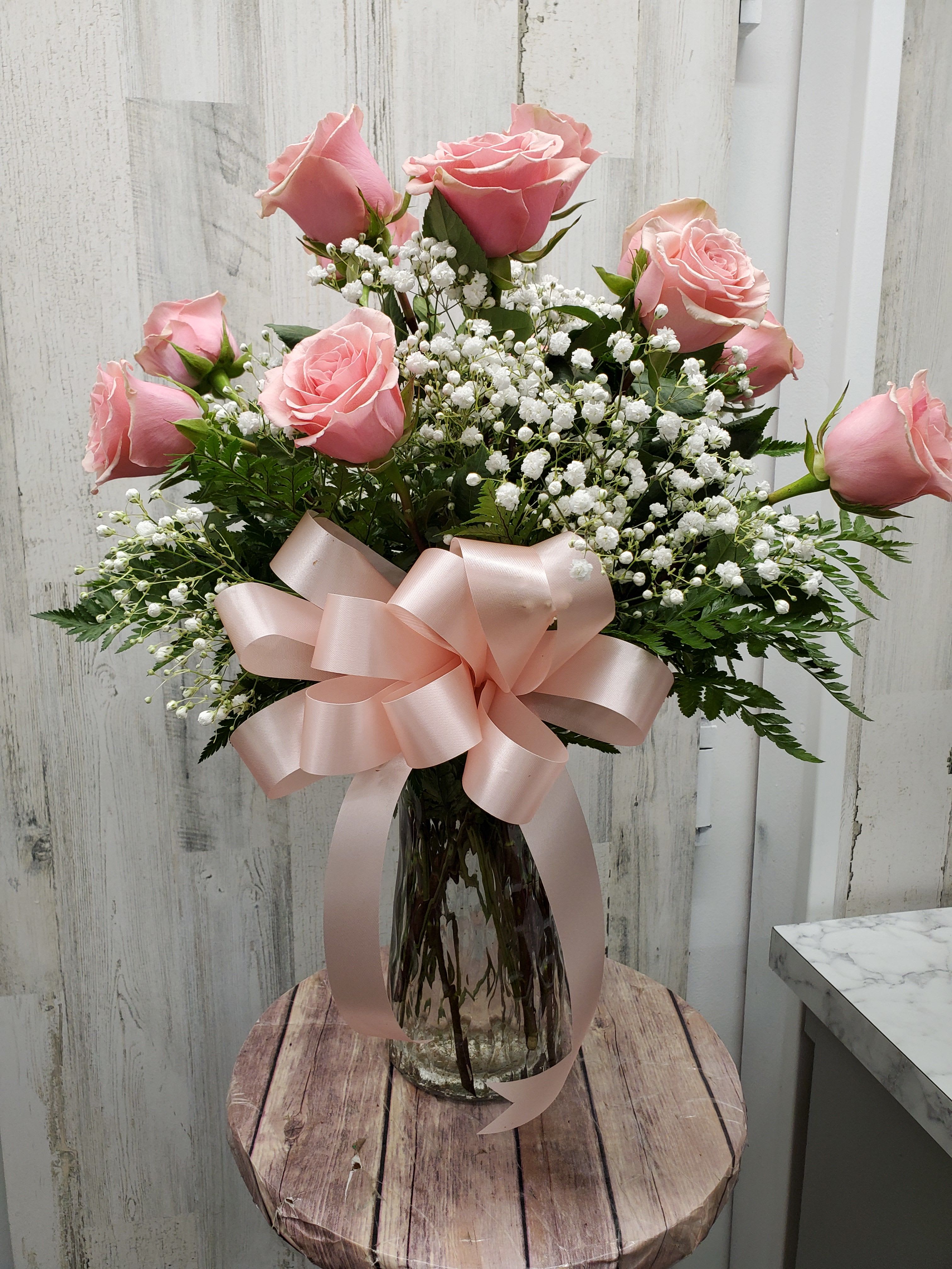 Pink roses in a glass vase with white baby's breath and a pink ribbon