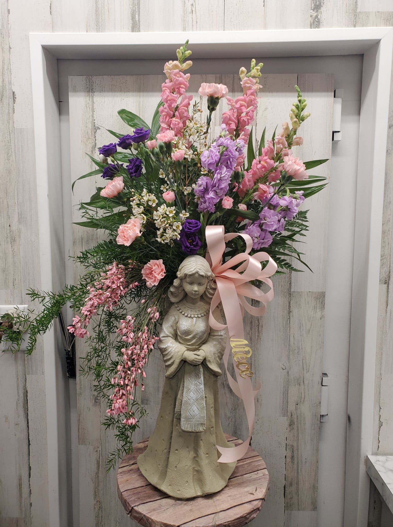 Tall floral arrangement with pink and purple blooms on a statue base