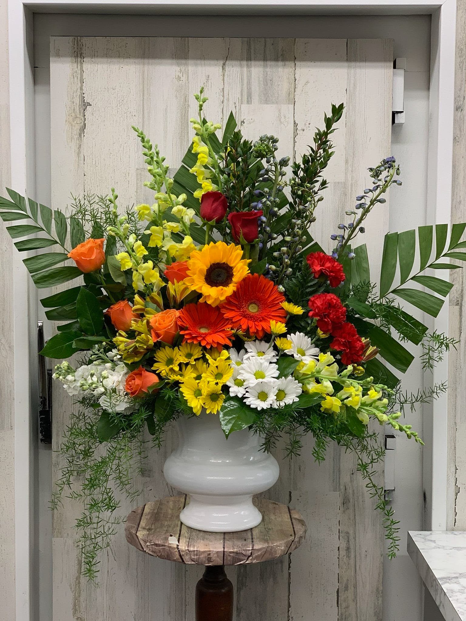 Large mixed flower arrangement in a white urn vase