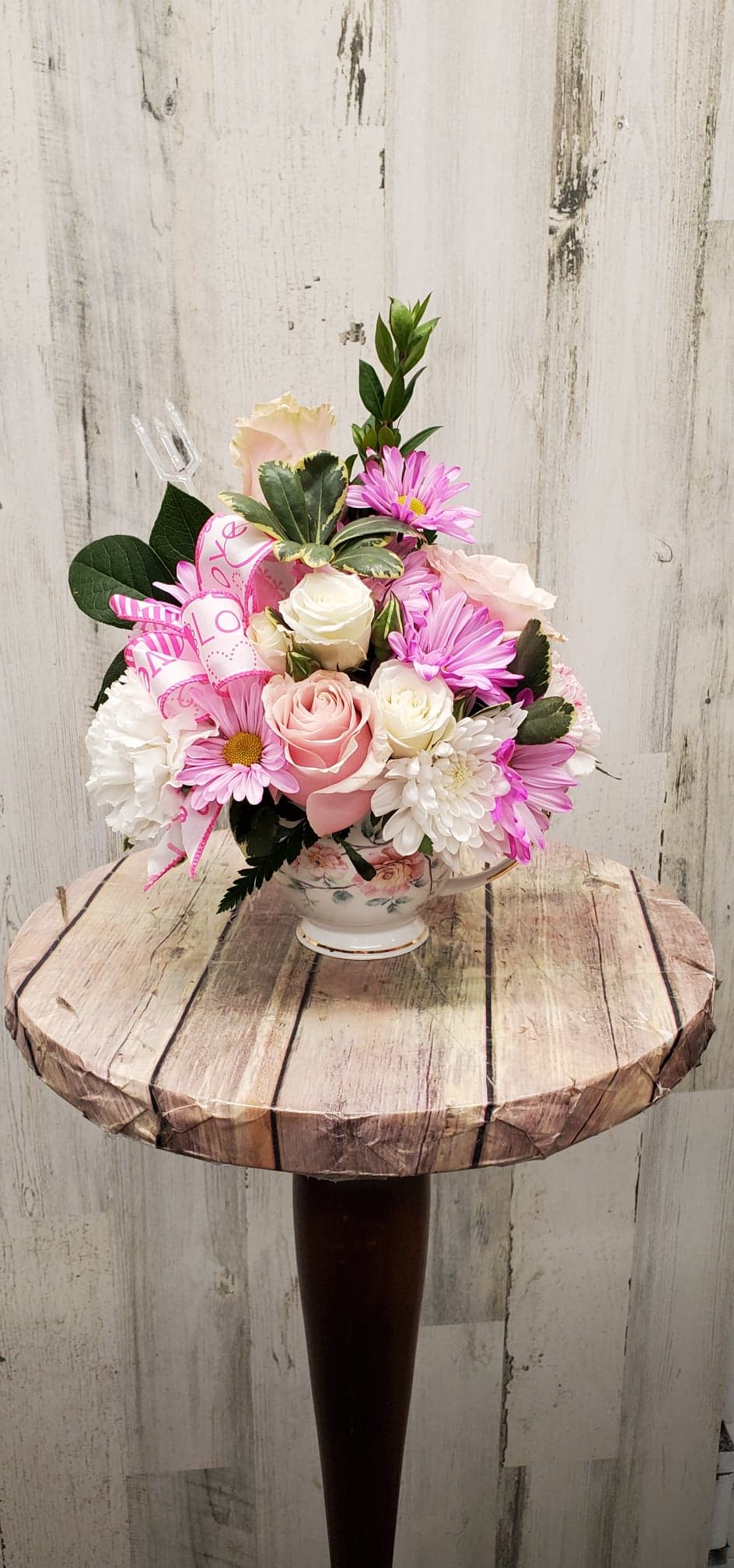 Pink and white flower arrangement in a floral teacup vase with a ribbon