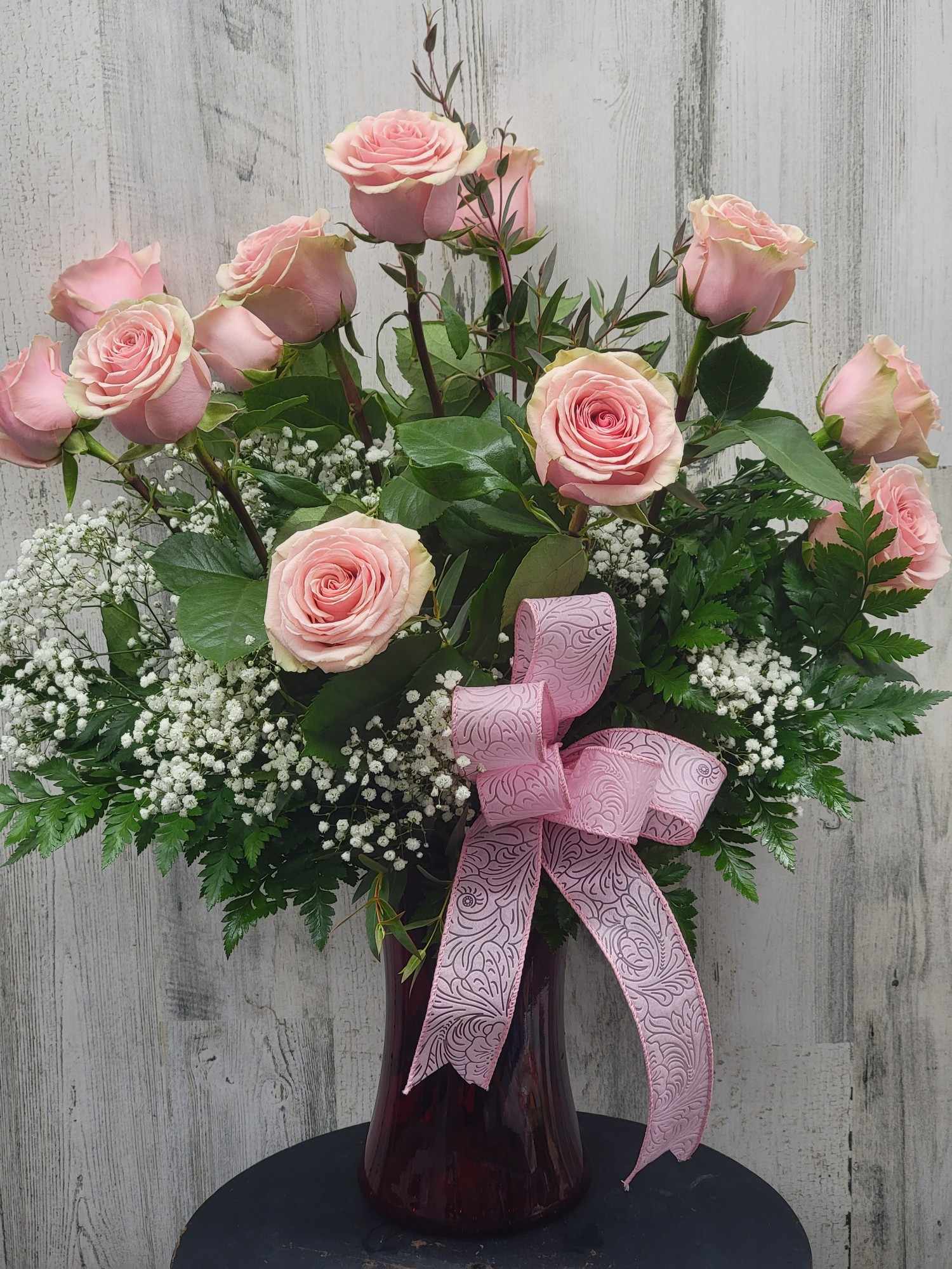Pink roses arranged in a dark glass vase with a pink ribbon