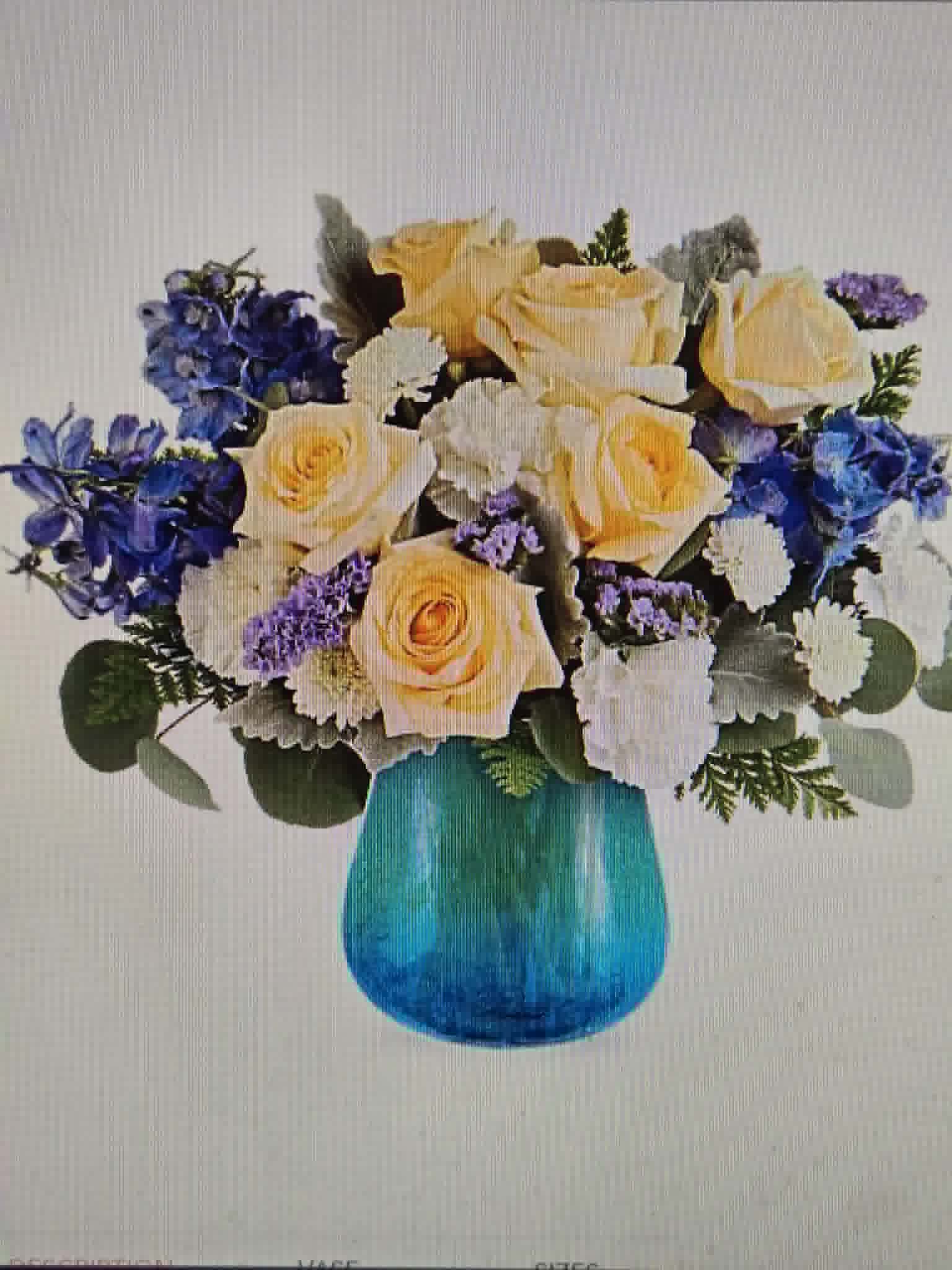 Mystic Waters - Pale yellow roses take center stage in this cheerful floral arrangement, their soft cream tones warmed by clusters of vivid blue and purple filler blooms and delicate white accents - a perfect birthday bouquet or celebratory arrangement to brighten someone's day. The mix of cool blues and purples around the edges gives the composition a fresh, modern energy that still feels gentle and inviting, ideal for saying "congratulations," "thinking of you," or "get well soon."  Arranged in a translucent blue glass vase, the rounded, full composition measures as a compact yet impactful display that suits a dining table, office desk, or bedside table. Textures range from the velvety roses to the airy filler flowers, creating visual depth and a softly layered scent. This is the kind of floral gift that makes the recipient feel noticed and celebrated; delivered ready-to-display with water already in the vase for immediate enjoyment.