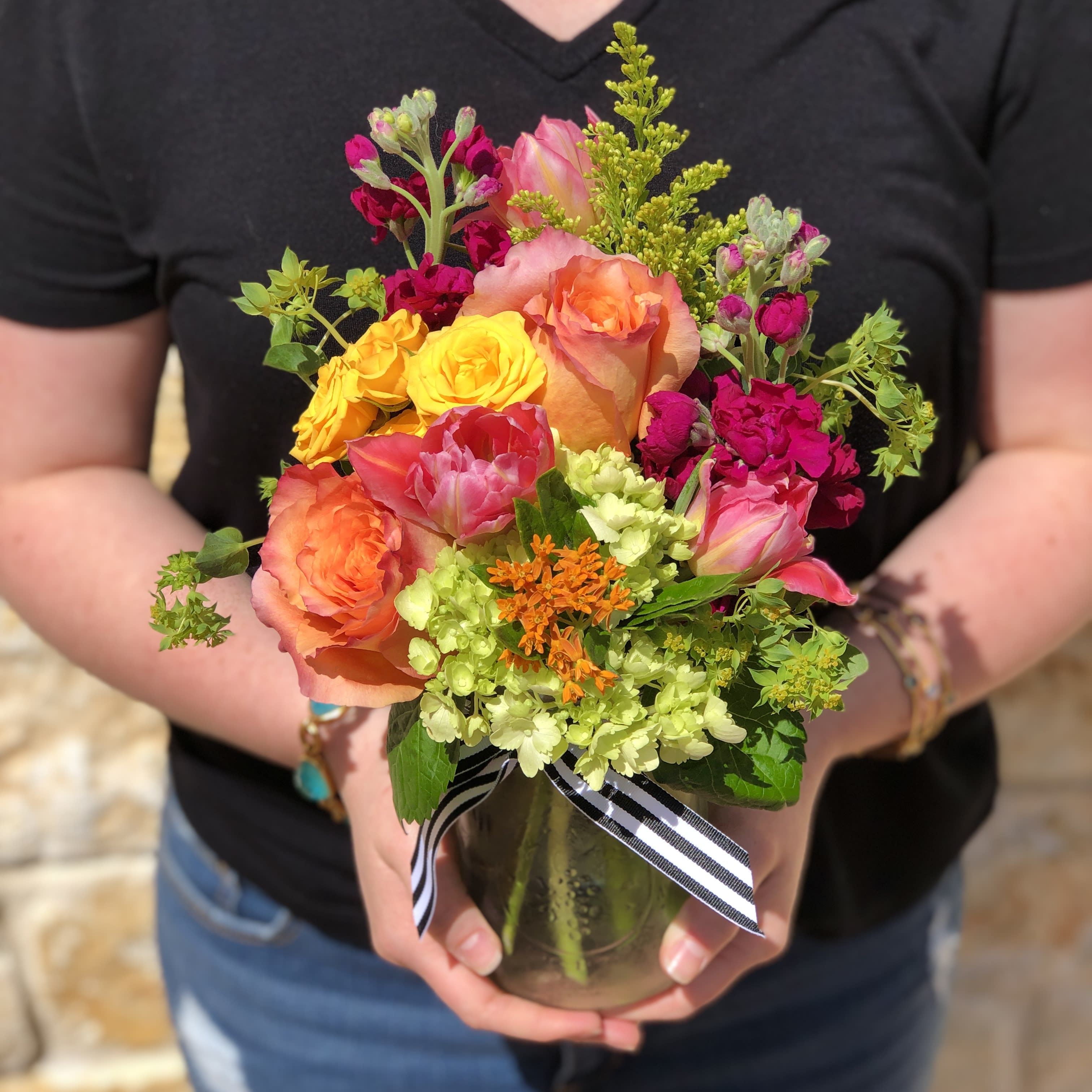 Colorful mixed bouquet of roses and other blooms in a glass vase with ribbon