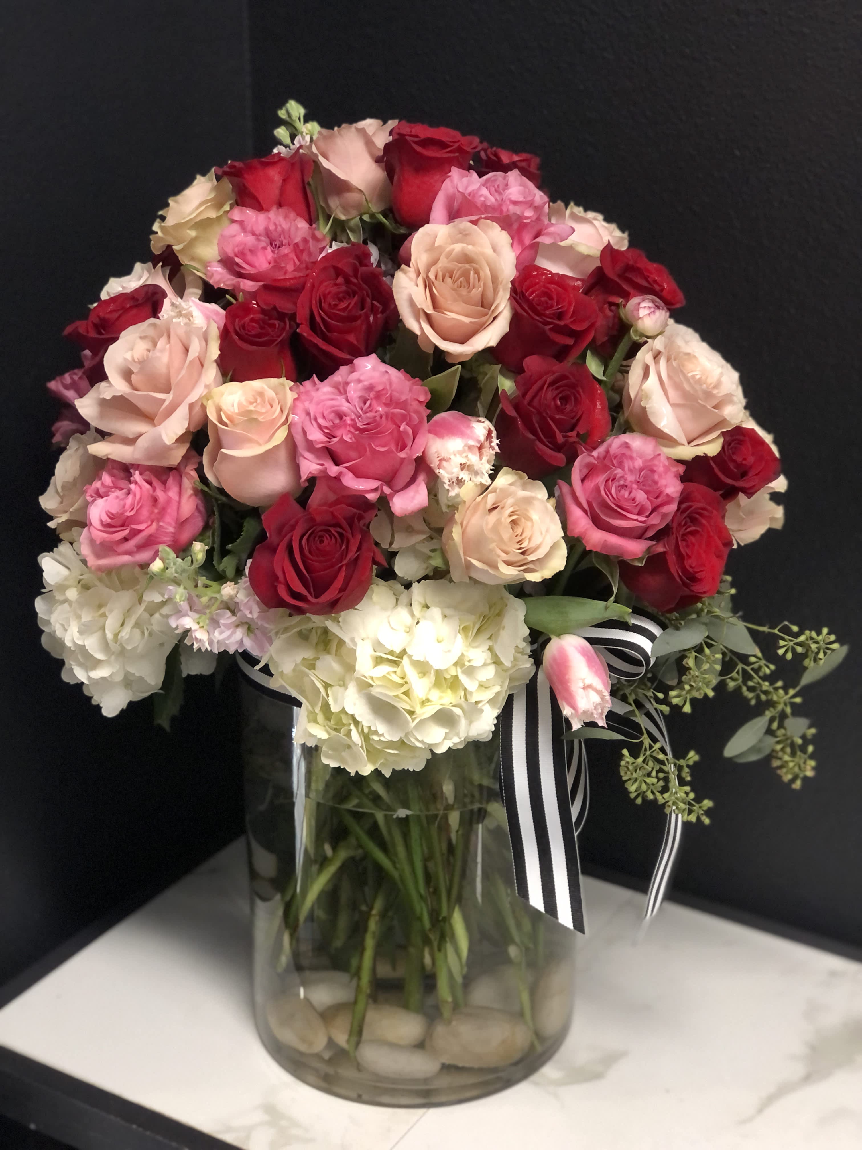 Bouquet of pink and red roses in a glass vase with a striped ribbon