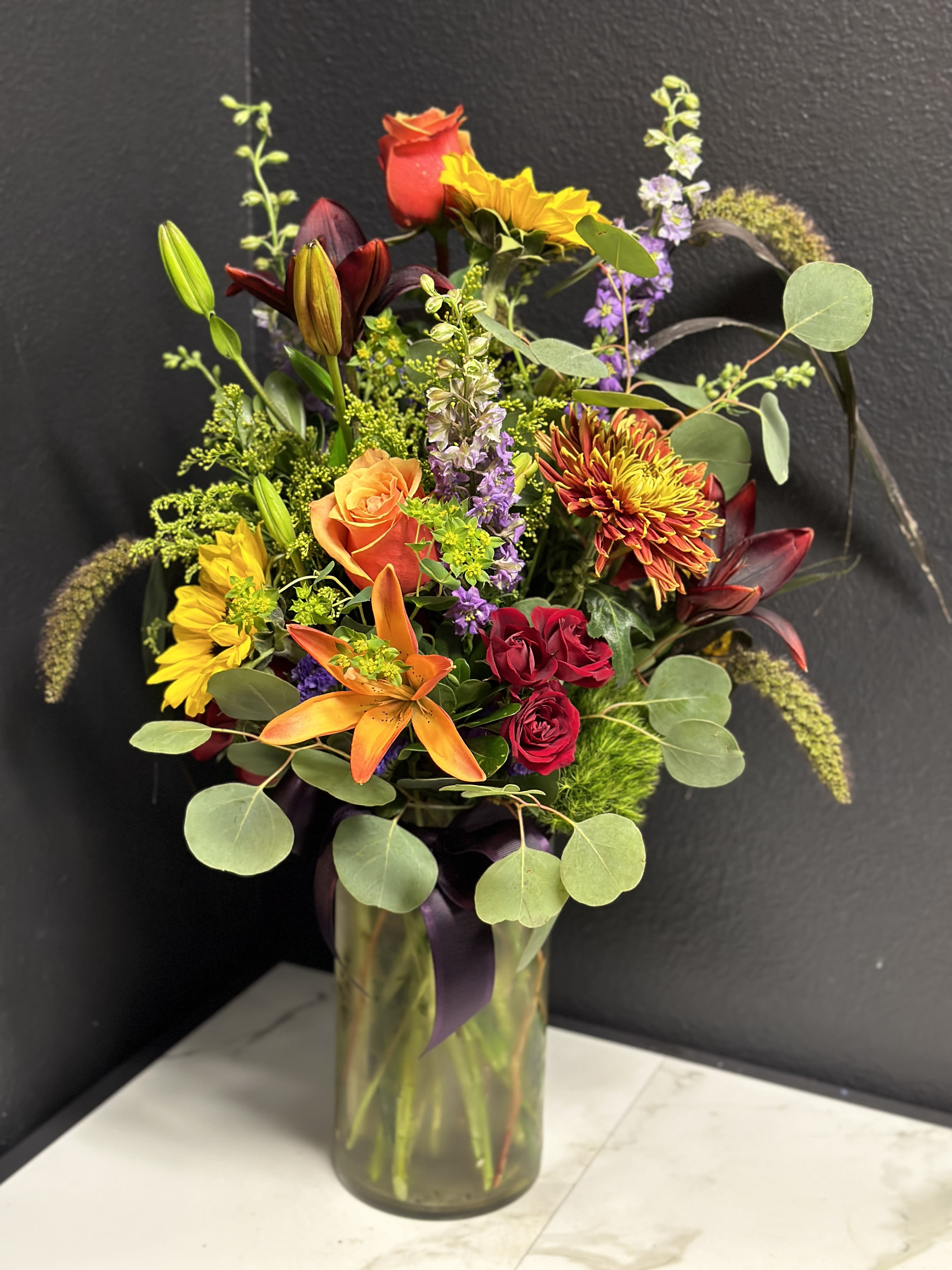 Mixed bouquet in a glass vase with roses, lilies, and sunflowers