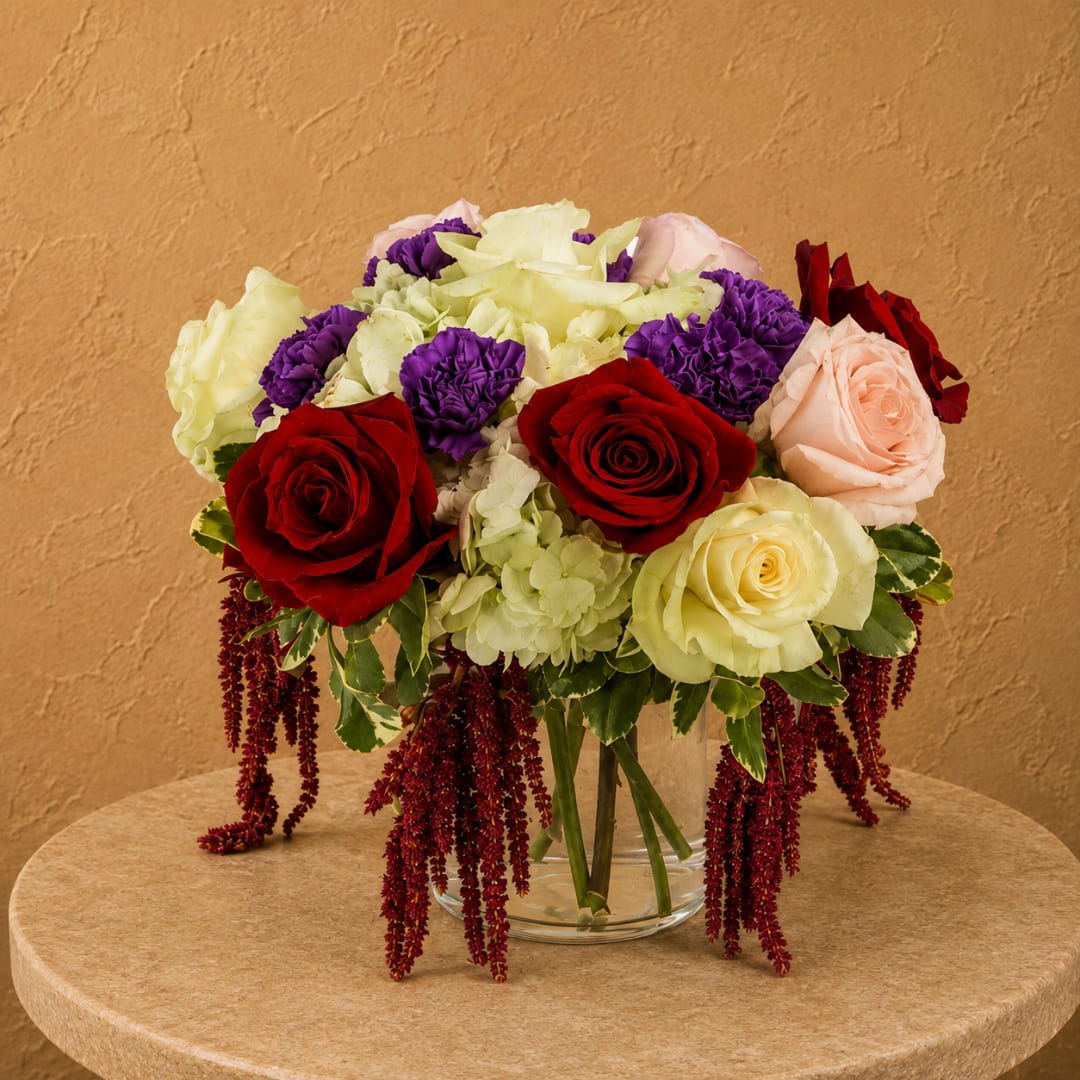 Mixed bouquet of roses, hydrangeas, and carnations in a clear glass vase