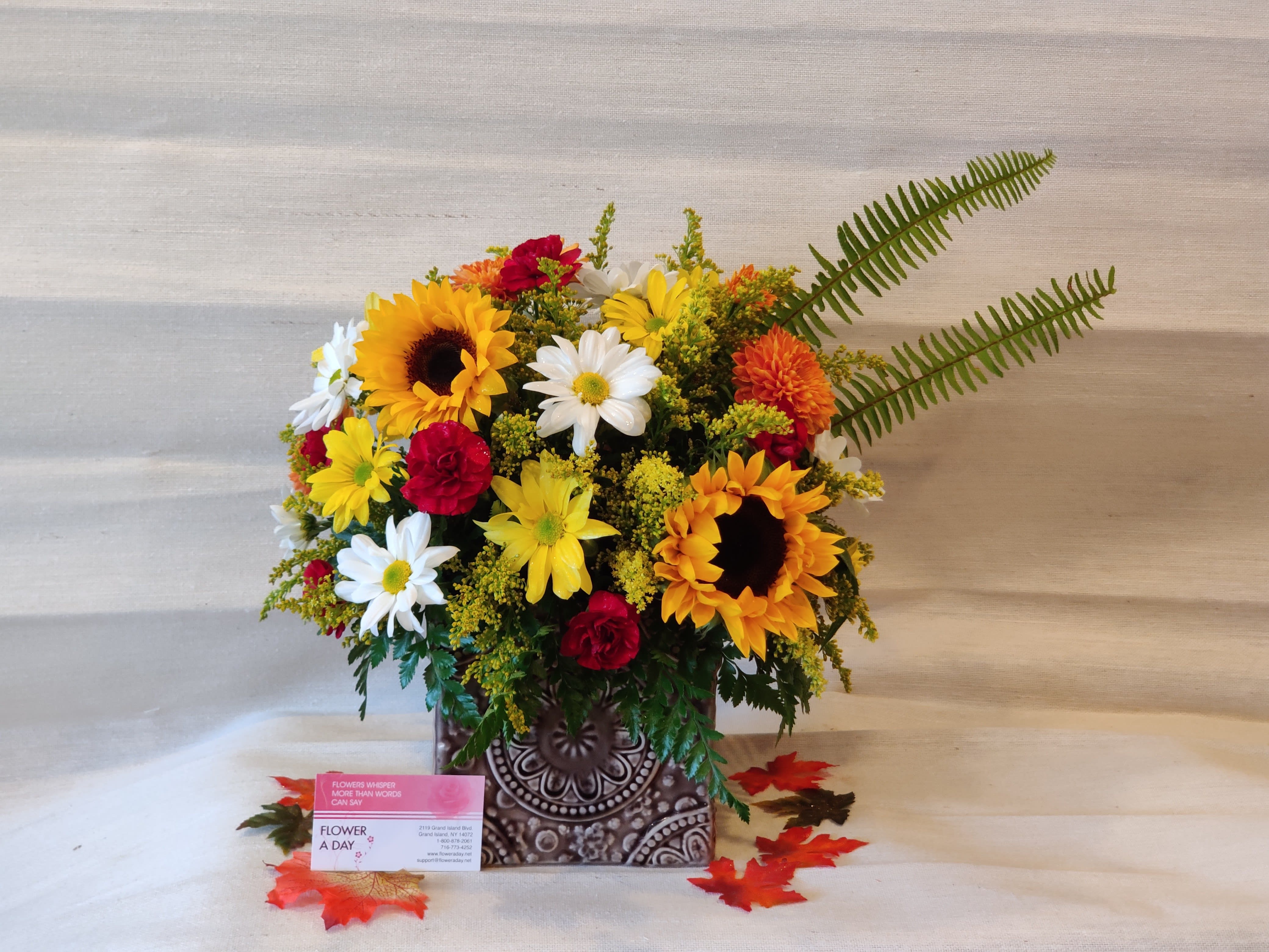 Mixed bouquet with sunflowers, daisies, and red carnations in a patterned vase